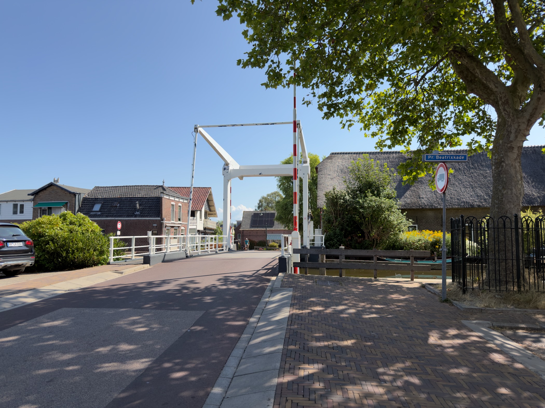 White drawbridge at Prinses Beatrixkade with thatched and brick houses under a clear blue sky