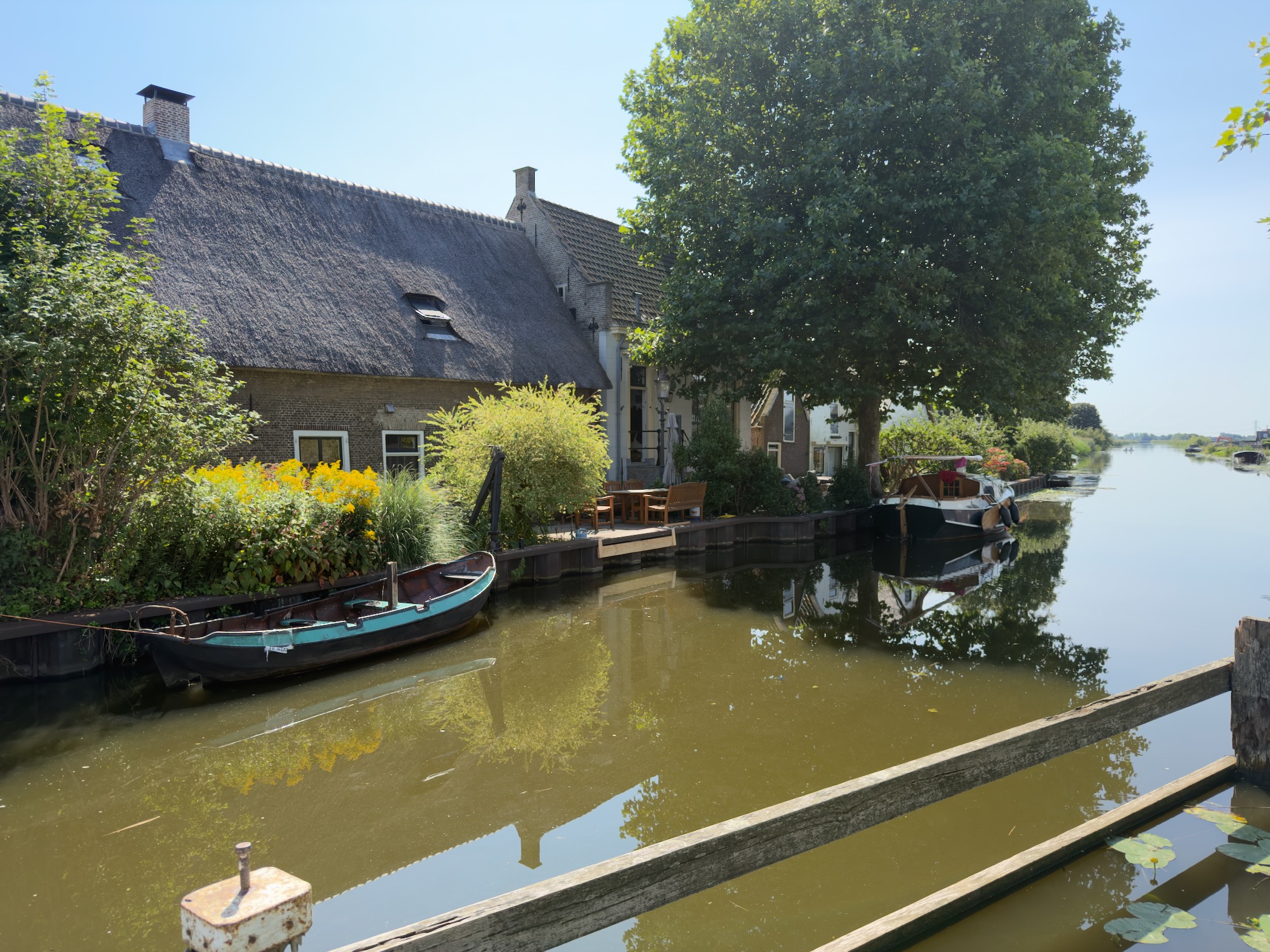 Thatched brick house and a small wooden boat on a canal lined with houses and a moored cabin cruiser