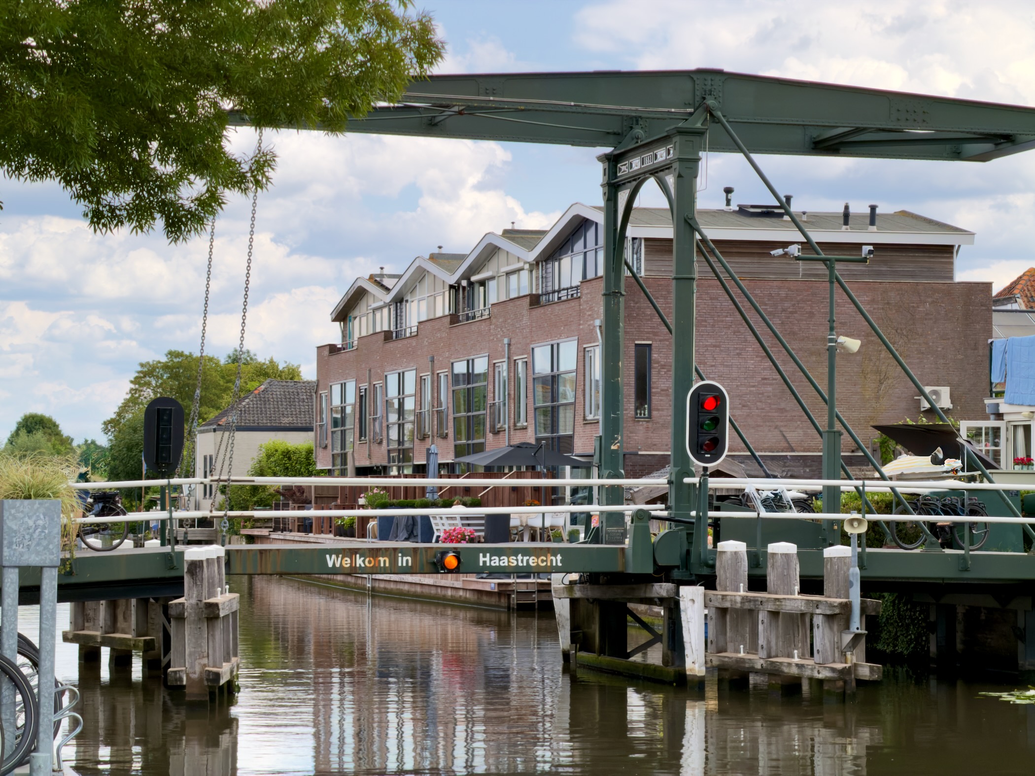 Green bascule bridge over a canal bearing the sign Welkom in Haastrecht, with brick apartments beyond
