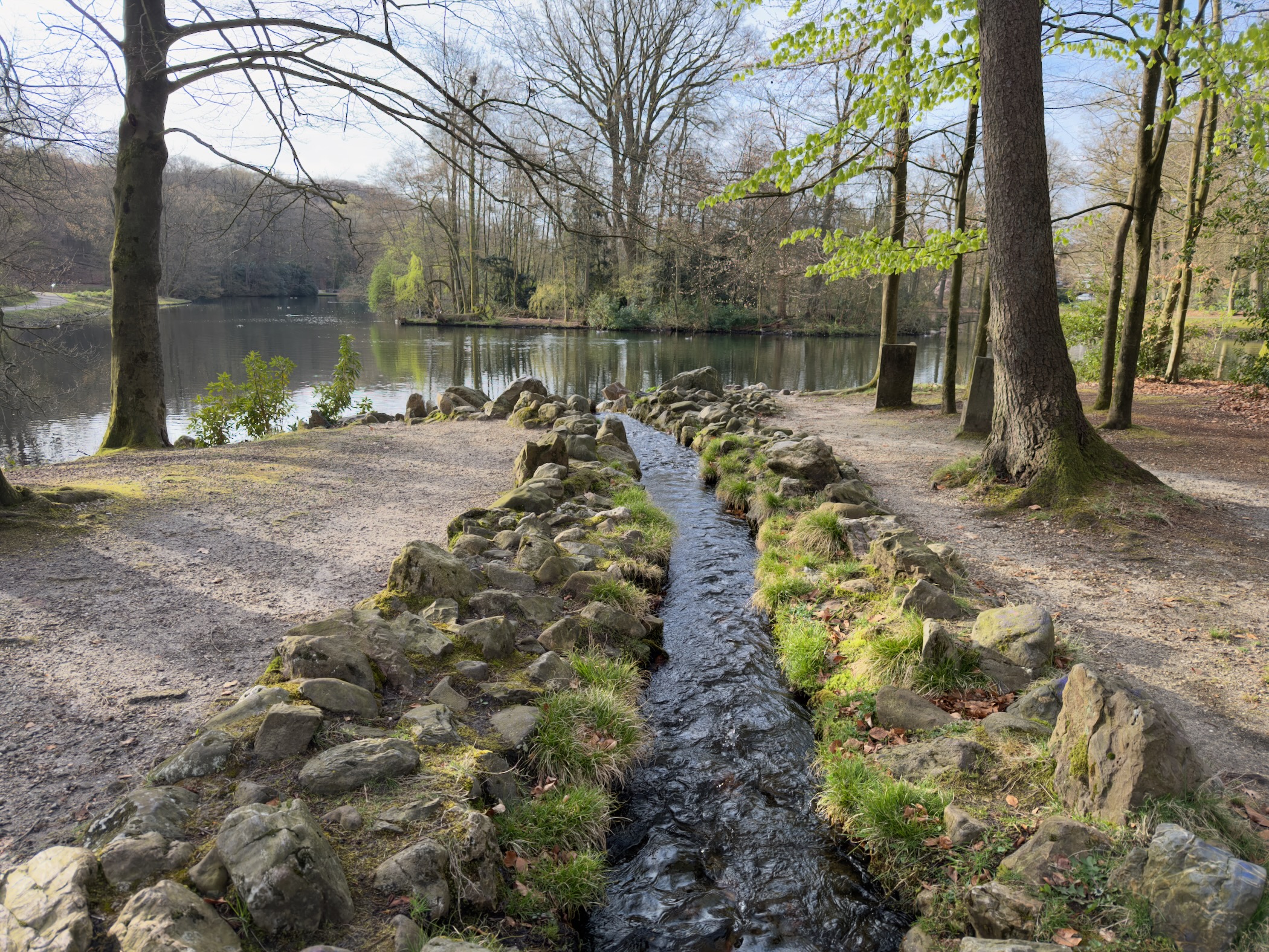 Stone-lined brook flowing into a pond in a wooded park