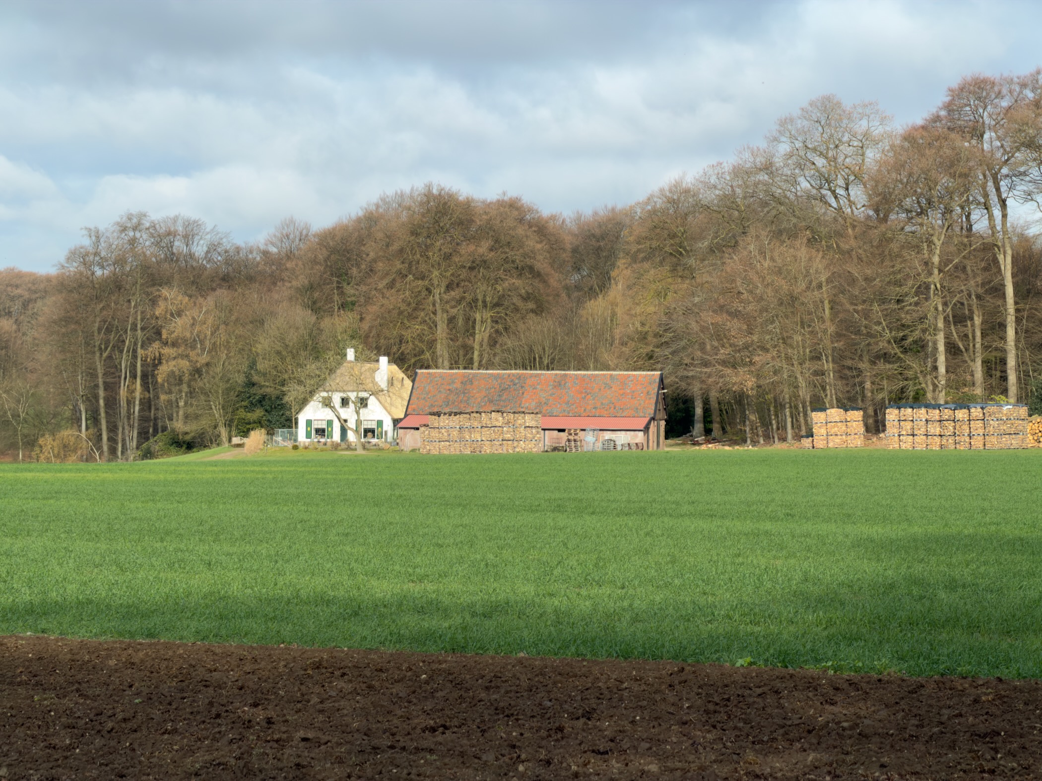 Farmhouse and barn with stacked hay bales at the edge of a green field