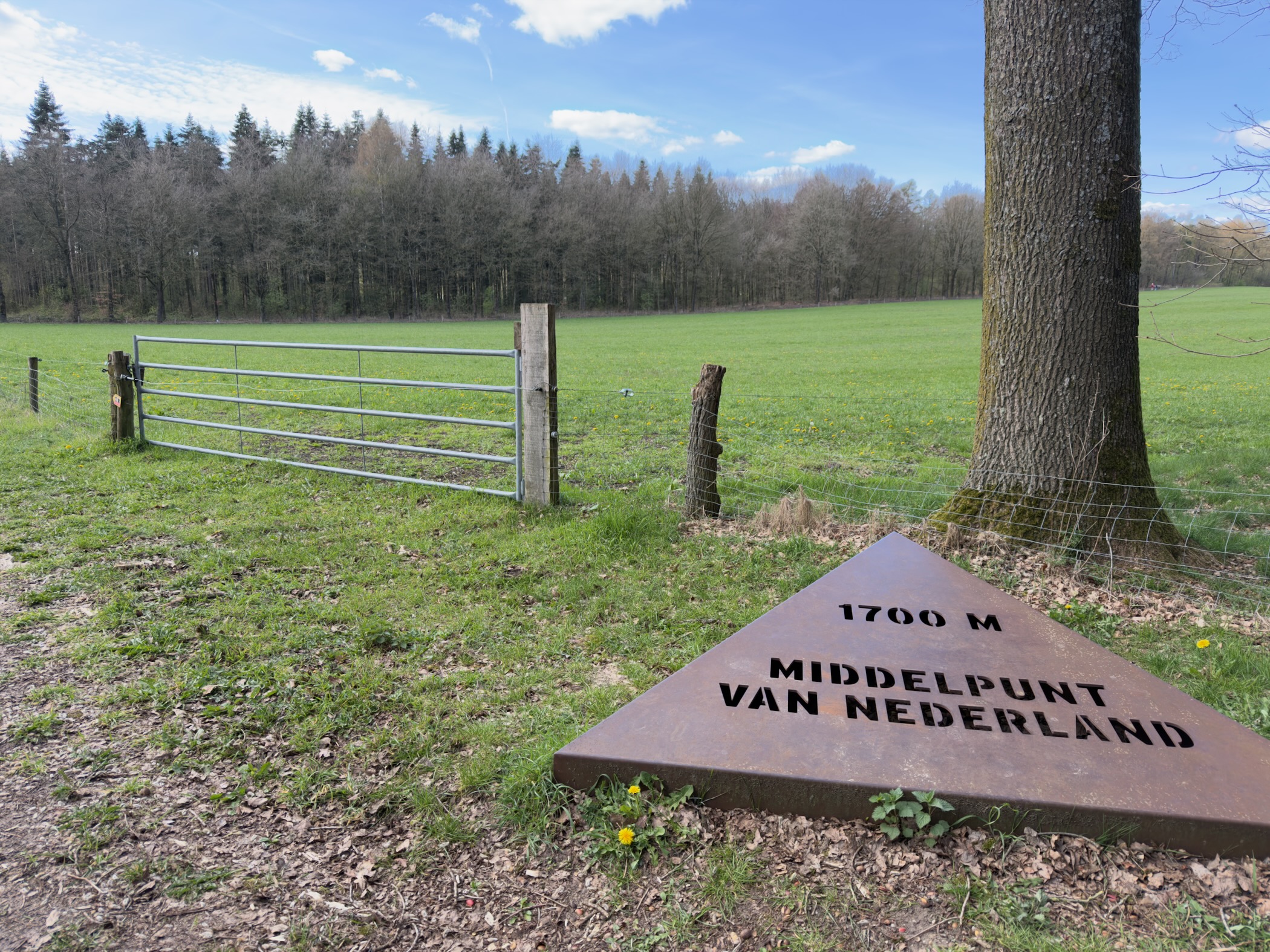 Stone marker reading 1700 M Middelpunt van Nederland near a green field