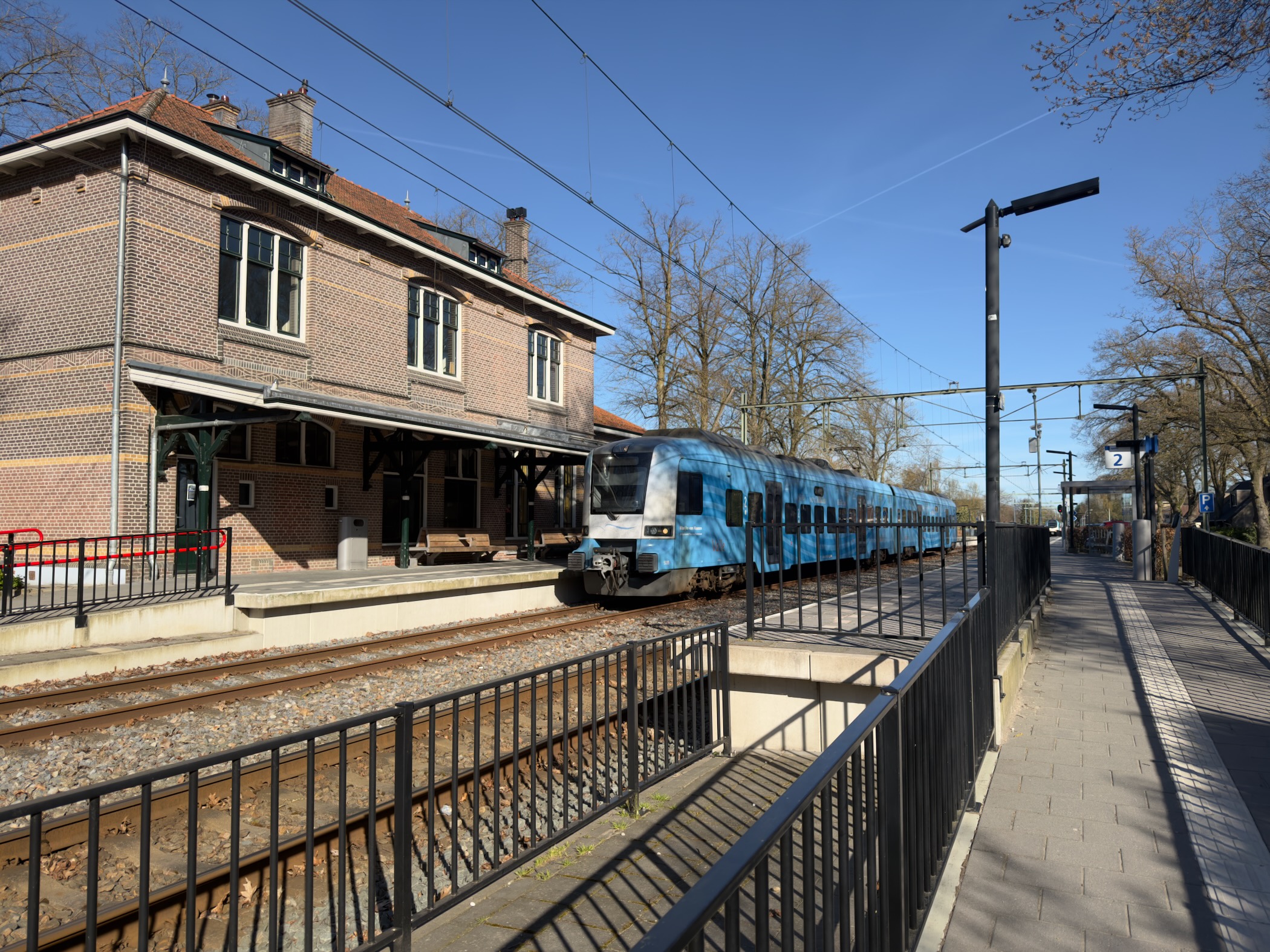Blue local train arriving at the brick station building of Lunteren