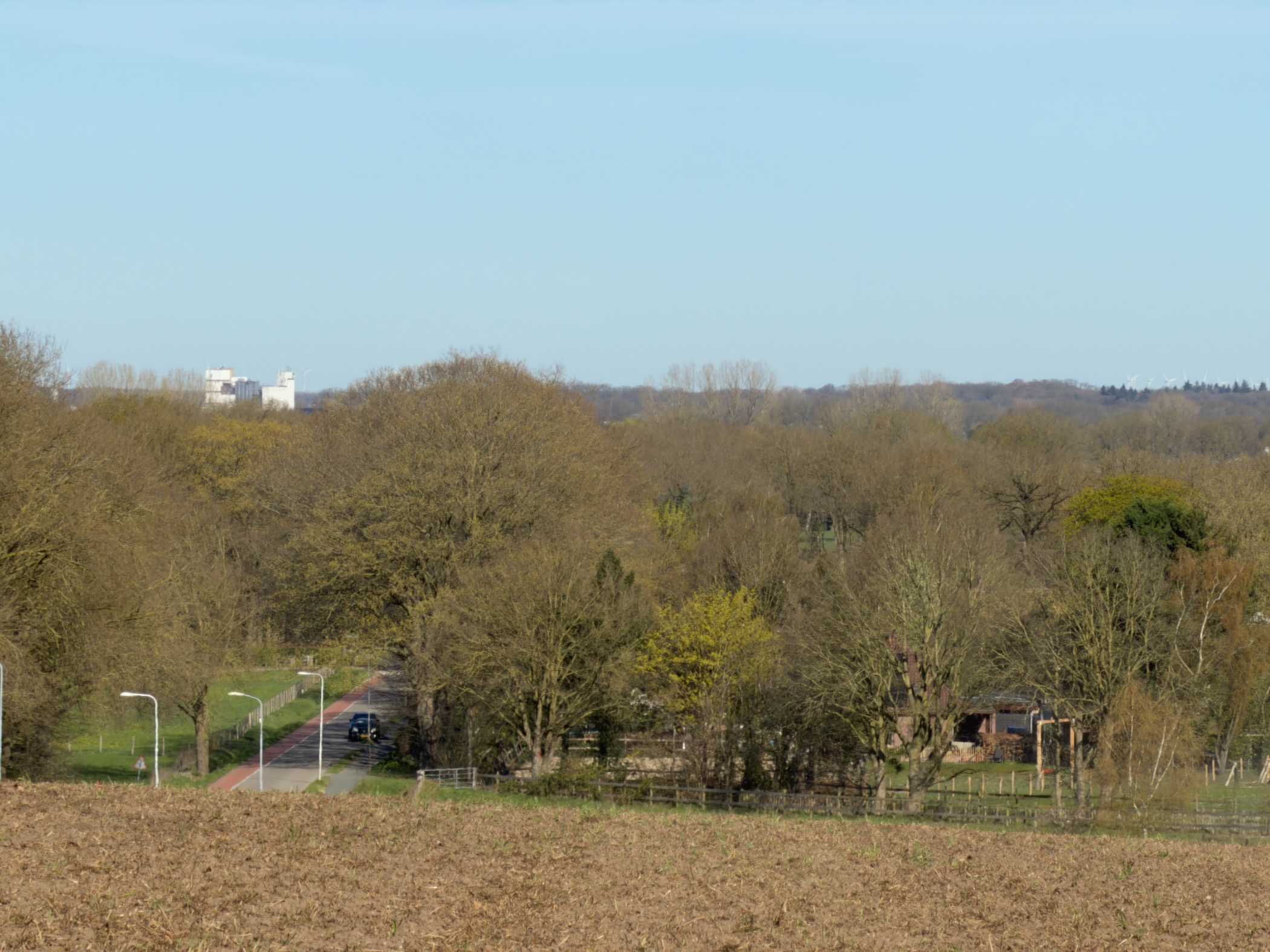 View across farmland toward distant water towers and bare trees