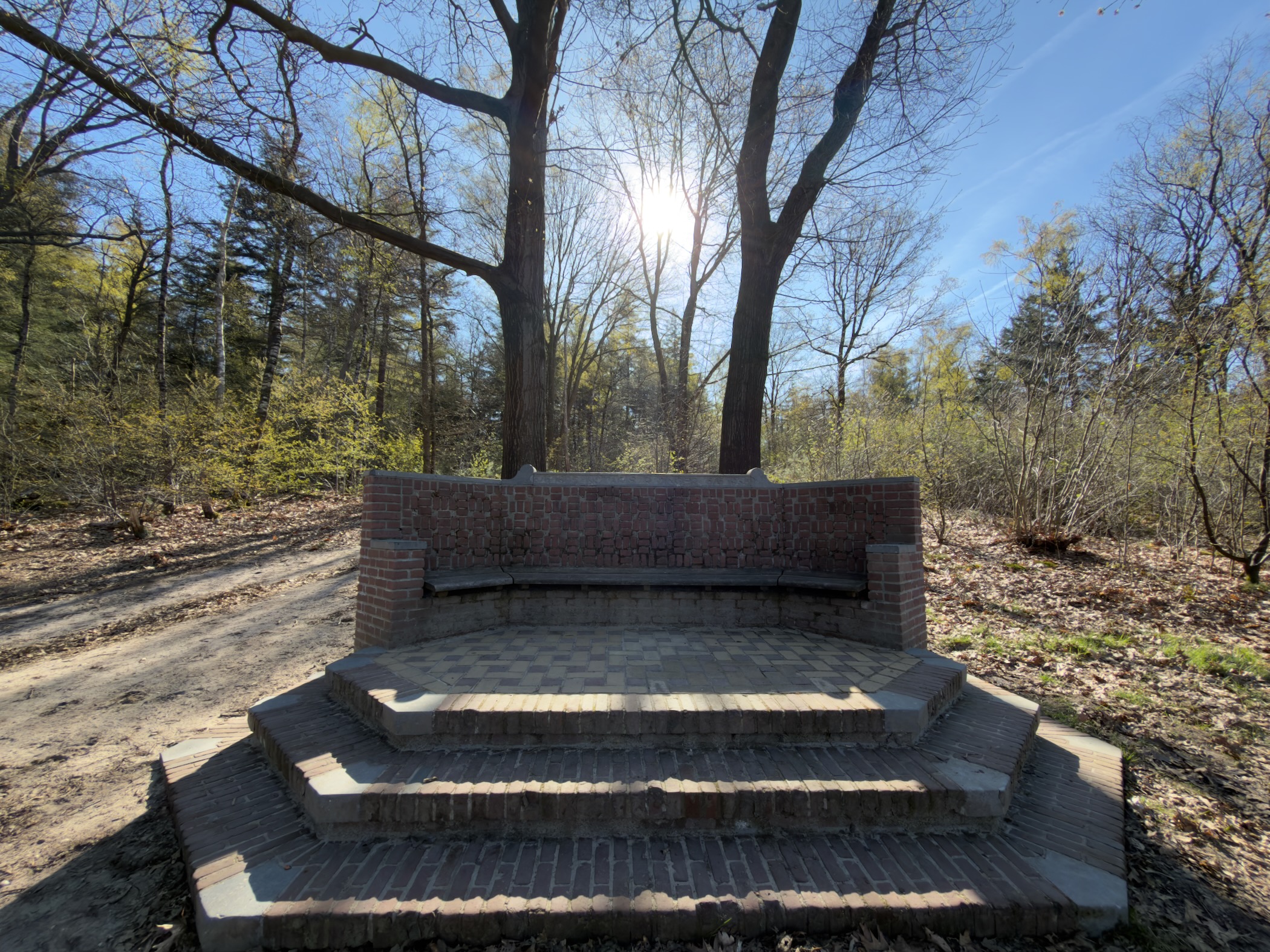 Brick monument with curved bench and stepped base in a forest clearing