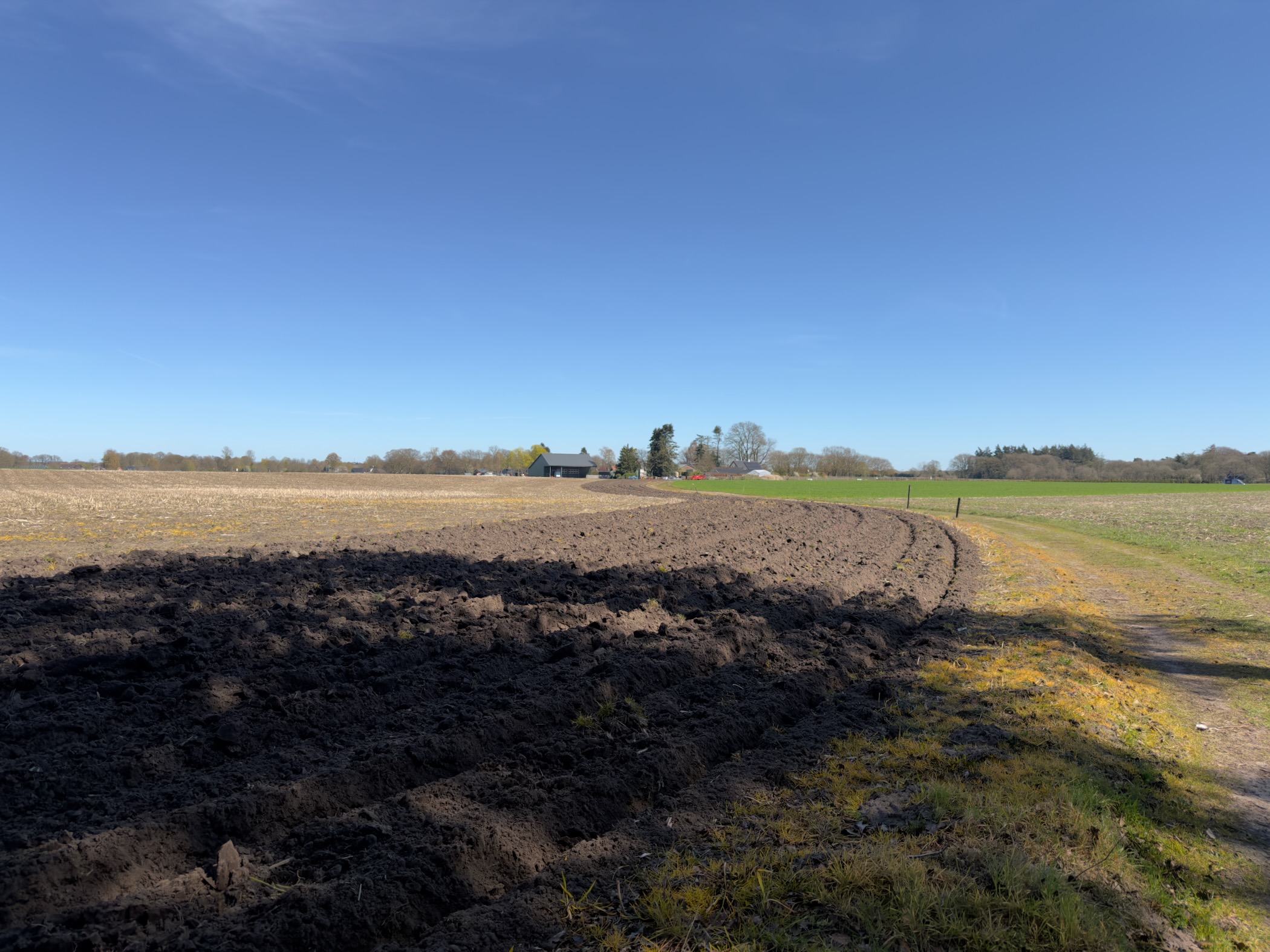 Freshly ploughed dark field with farm buildings on the horizon