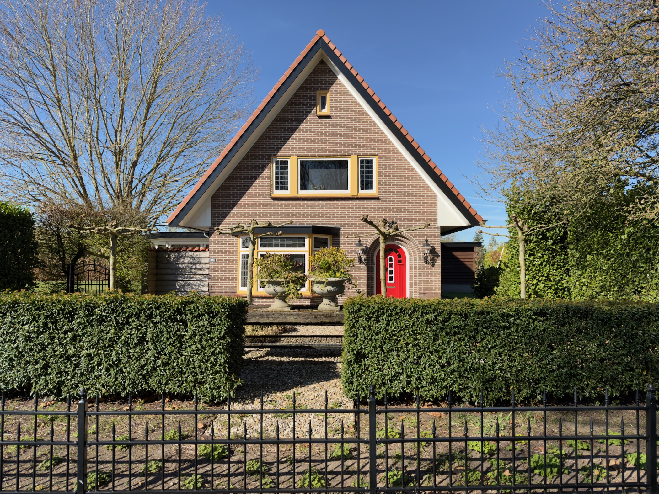 Detached house with a bright red front door behind a green privet hedge