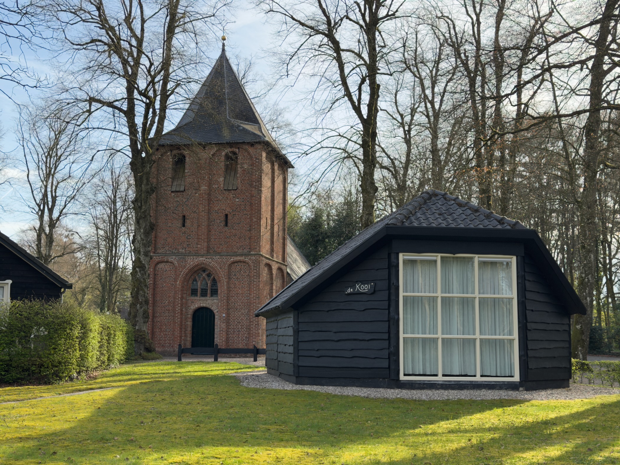 Medieval brick church tower and a small black wooden building in Kootwijk