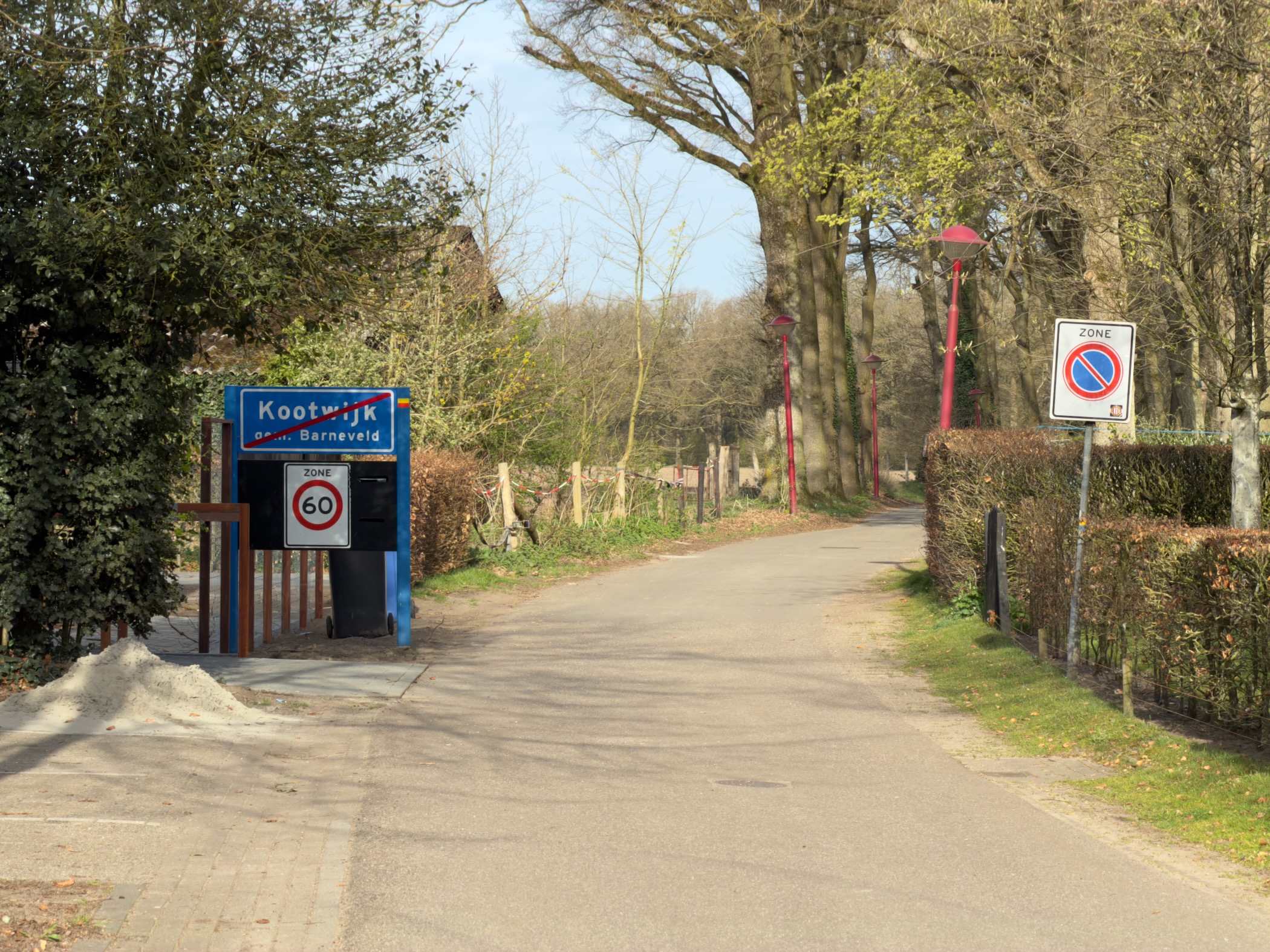 Kootwijk village sign with speed limit and a tree-lined road