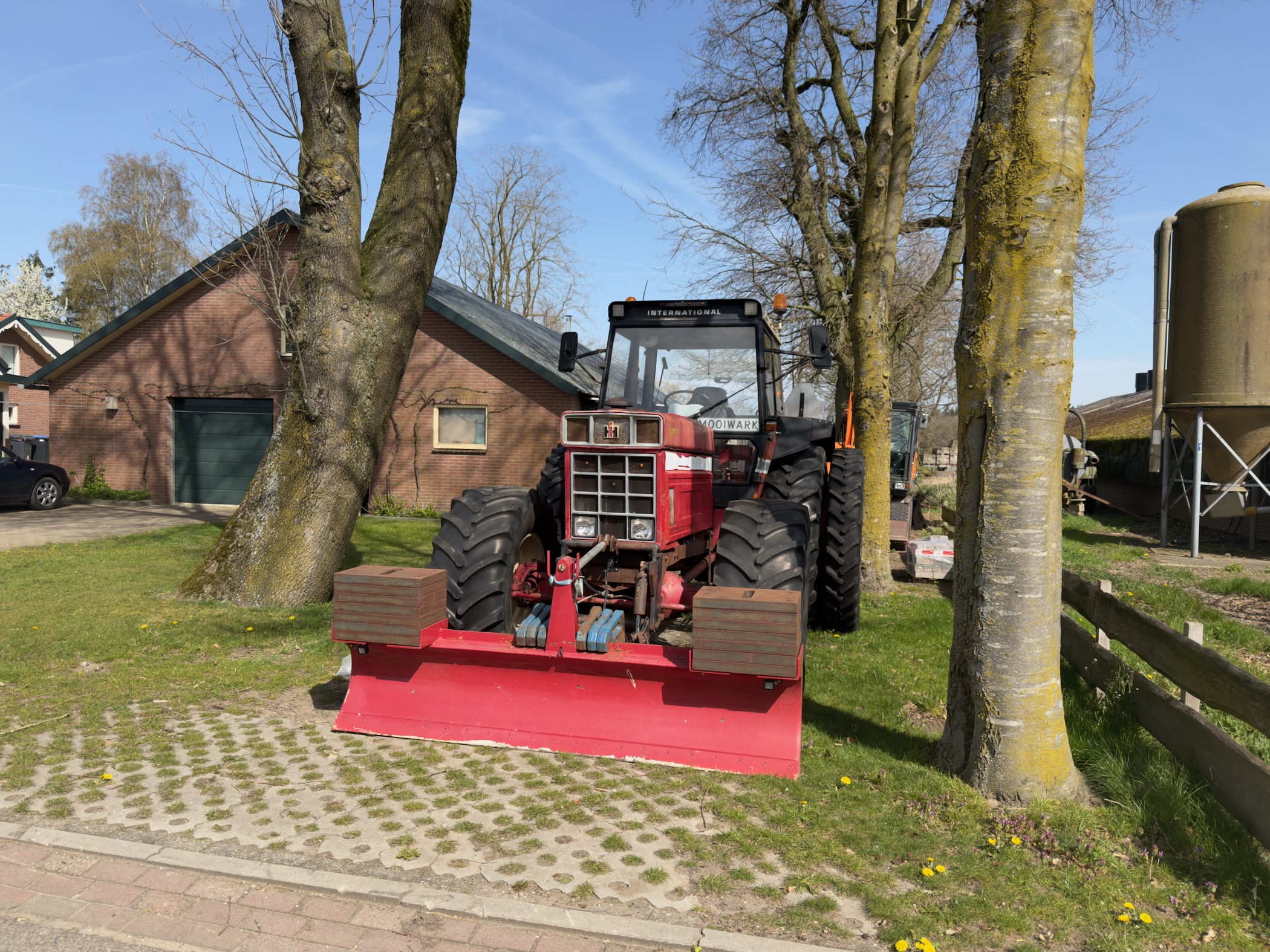 Red tractor with a front blade parked at a farm between trees