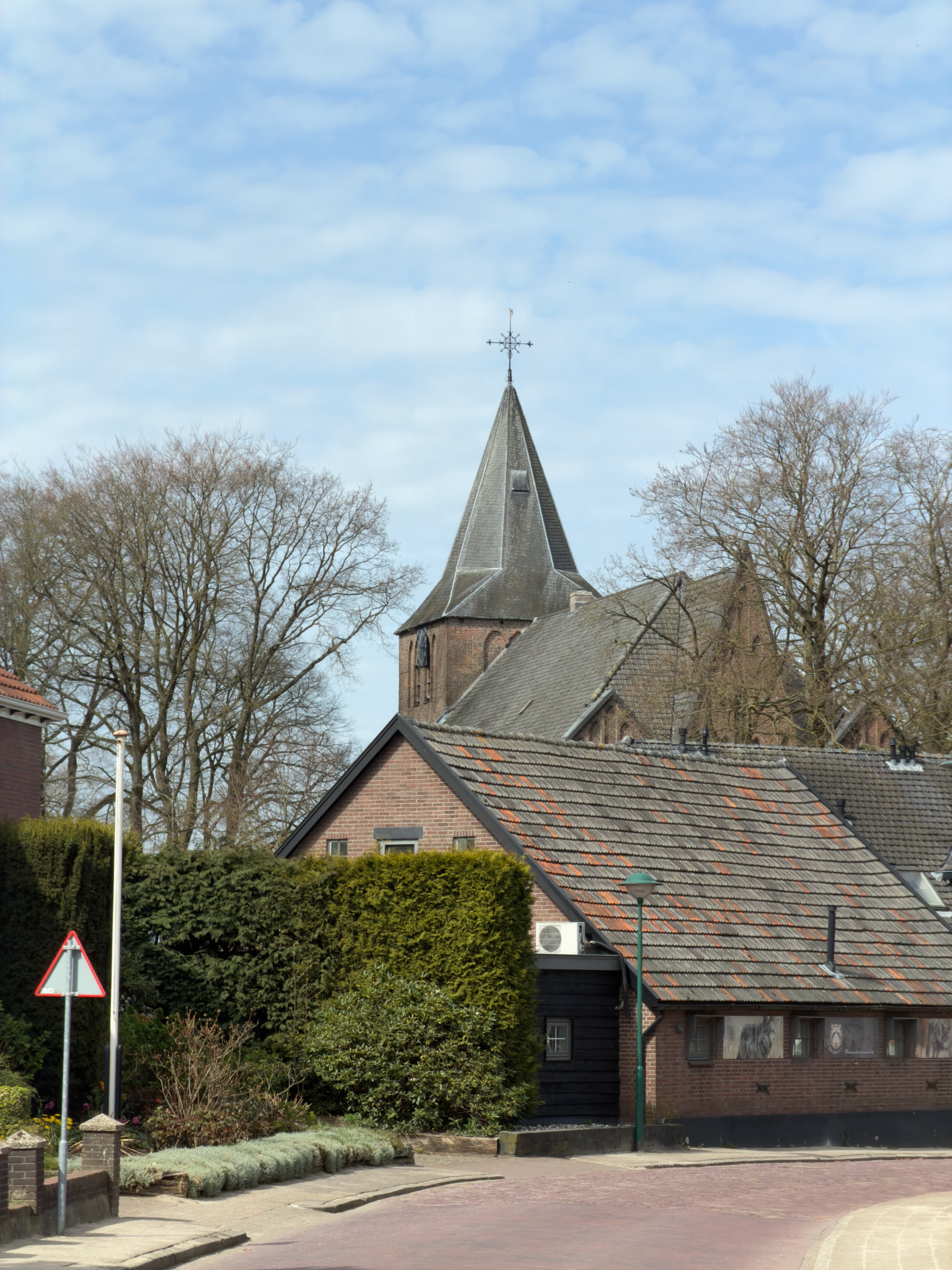 Church tower with a pointed spire rising above brick houses in Garderen