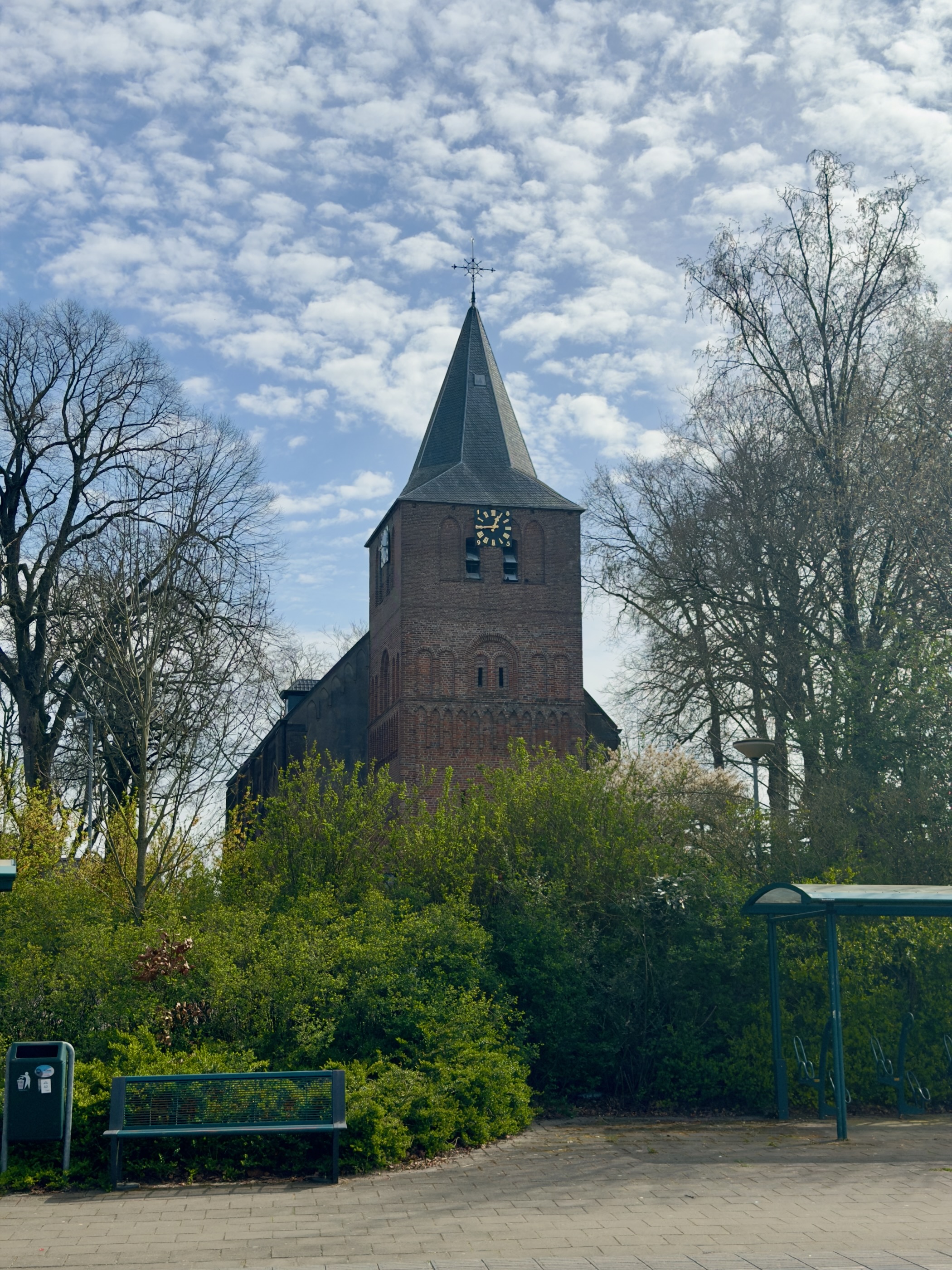 Medieval brick church tower of Garderen behind spring greenery and a bench