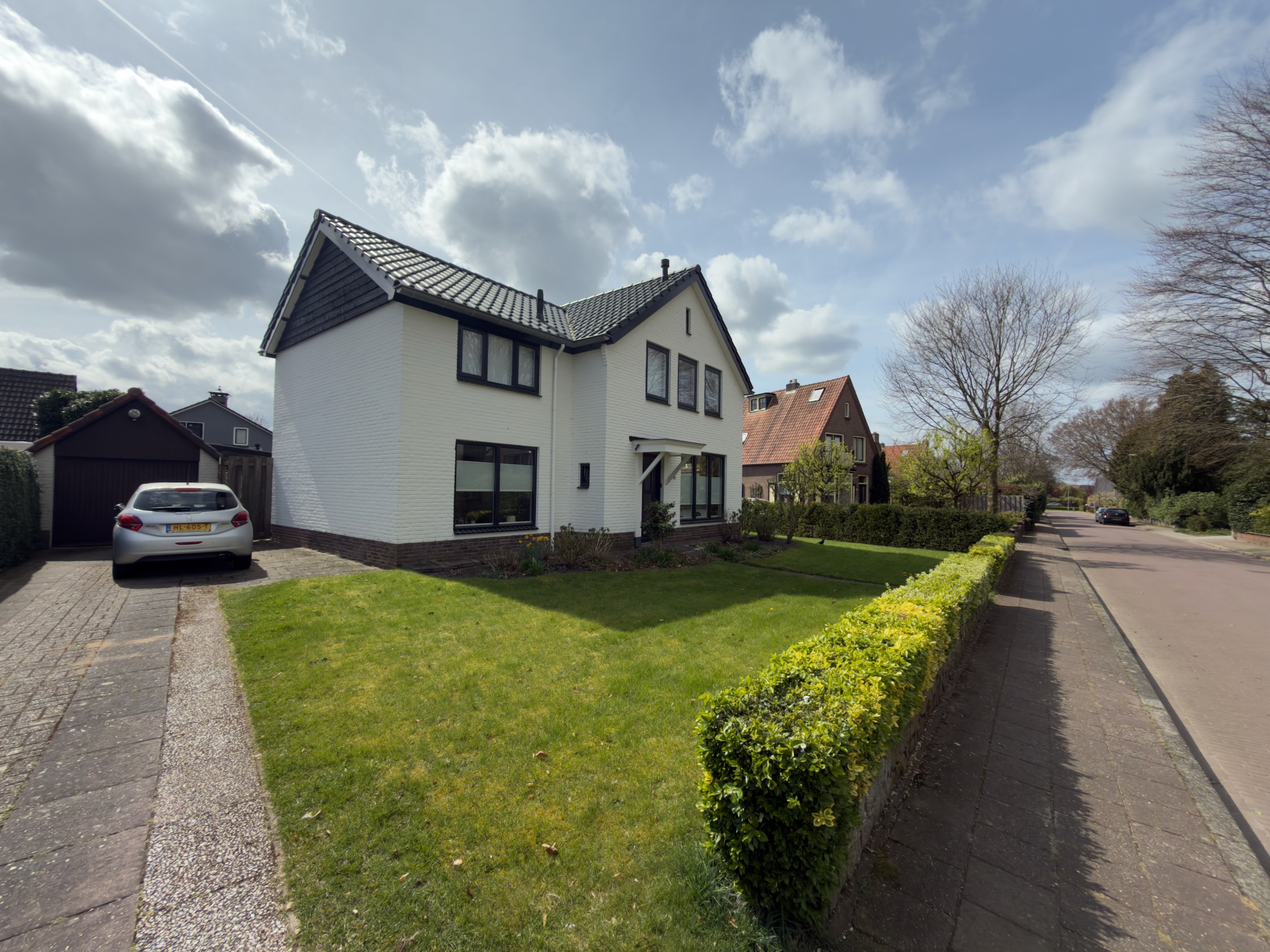 White detached house with a boxwood hedge on a quiet village street