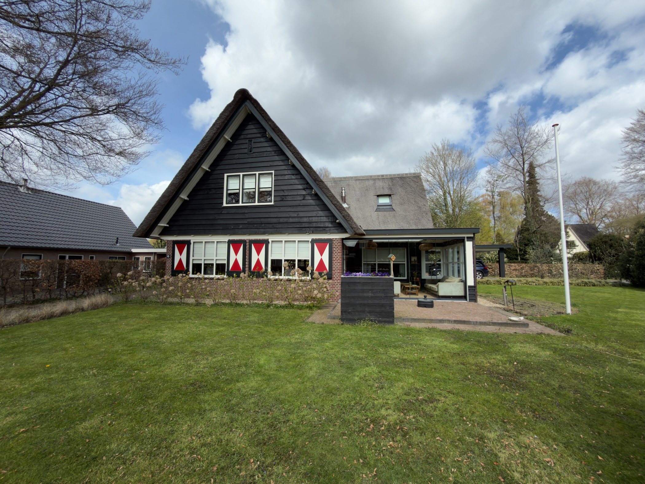 Dark wooden farmhouse with red-and-white shutters on a green lawn