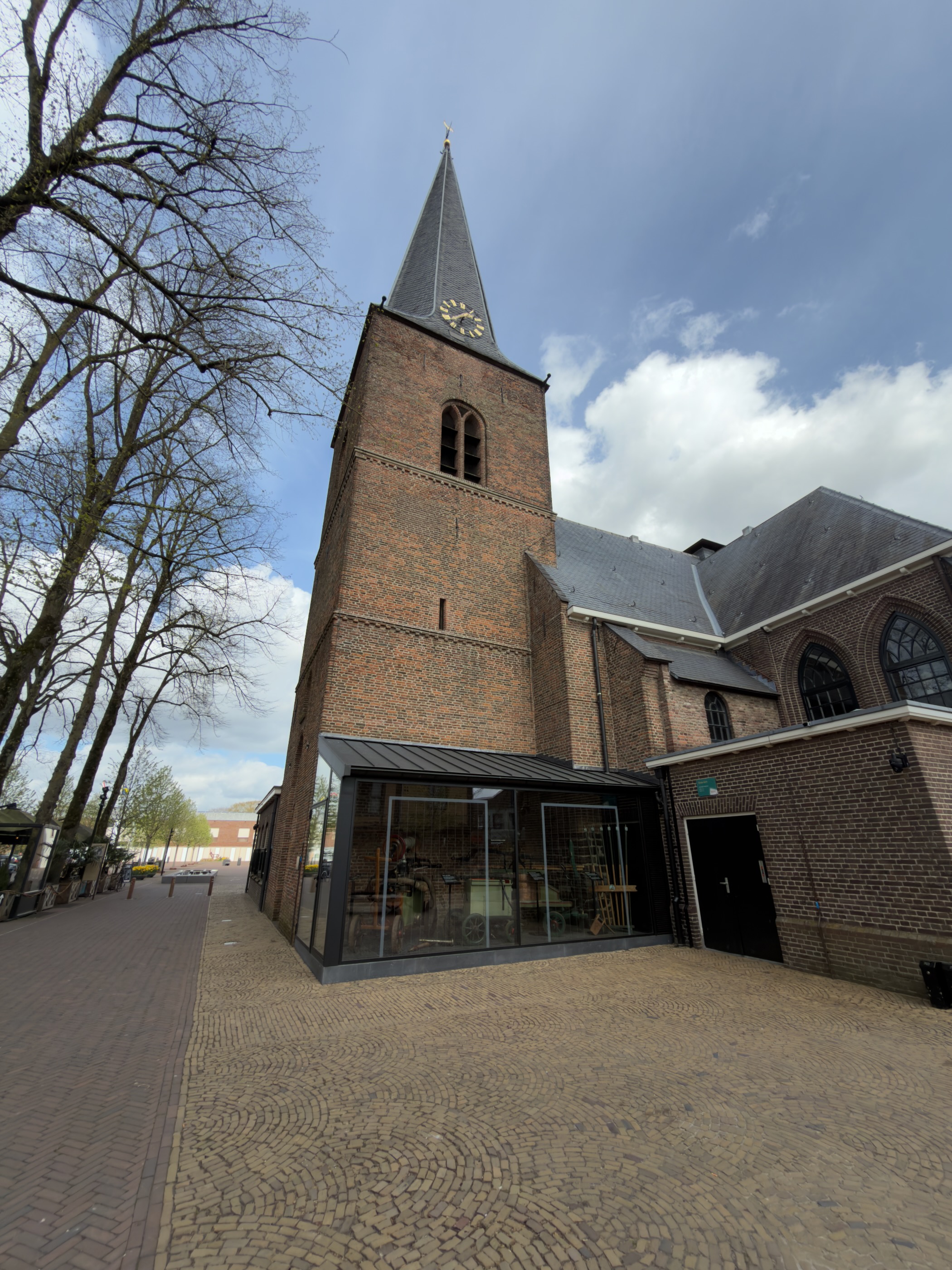 Tall brick church tower with a clock and glass entrance in Putten