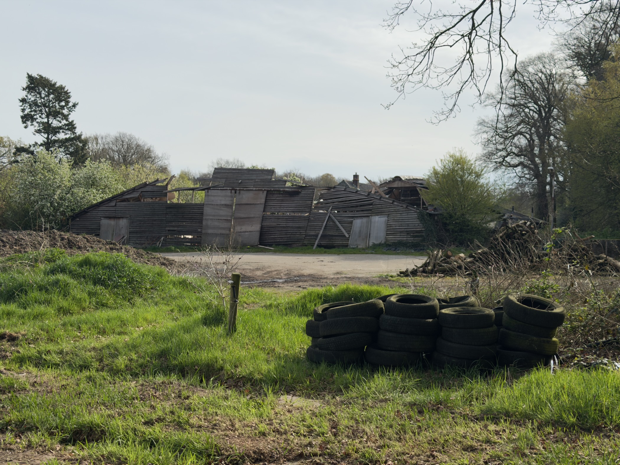 Dilapidated wooden barn with stacked tyres on a grassy farmyard