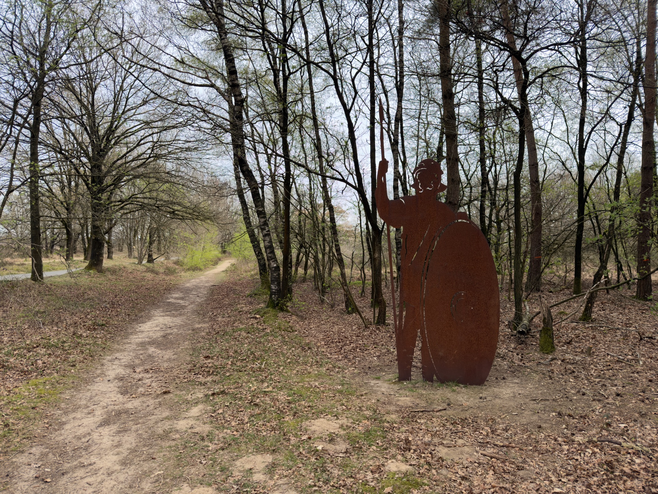 Rusted iron silhouette sculpture of a figure beside a forest trail