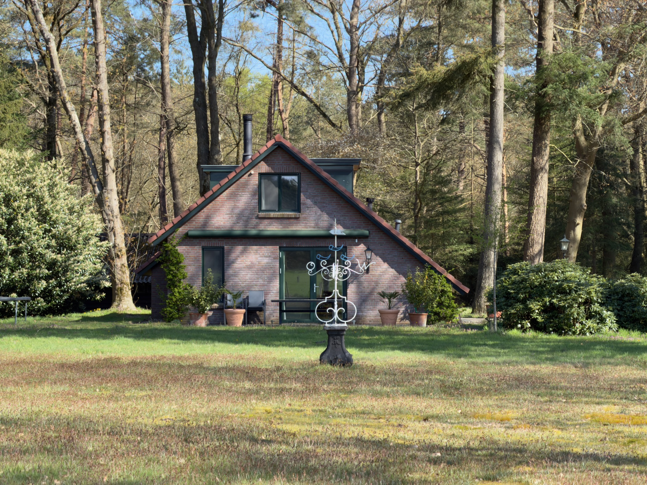 Brick cottage with a decorative iron fountain on a shaded woodland clearing