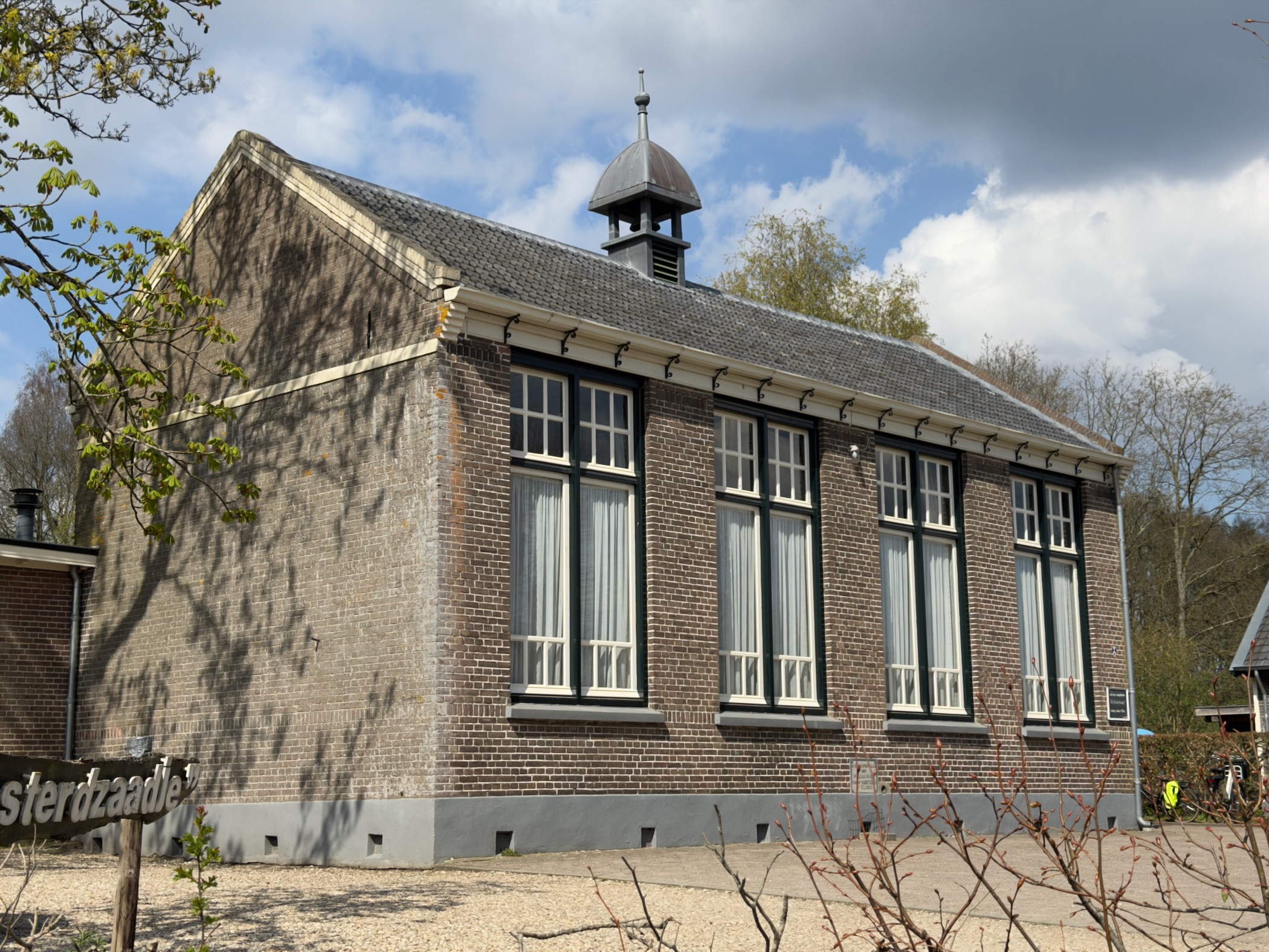 Brick schoolhouse with tall windows and a small bell tower under a cloudy sky