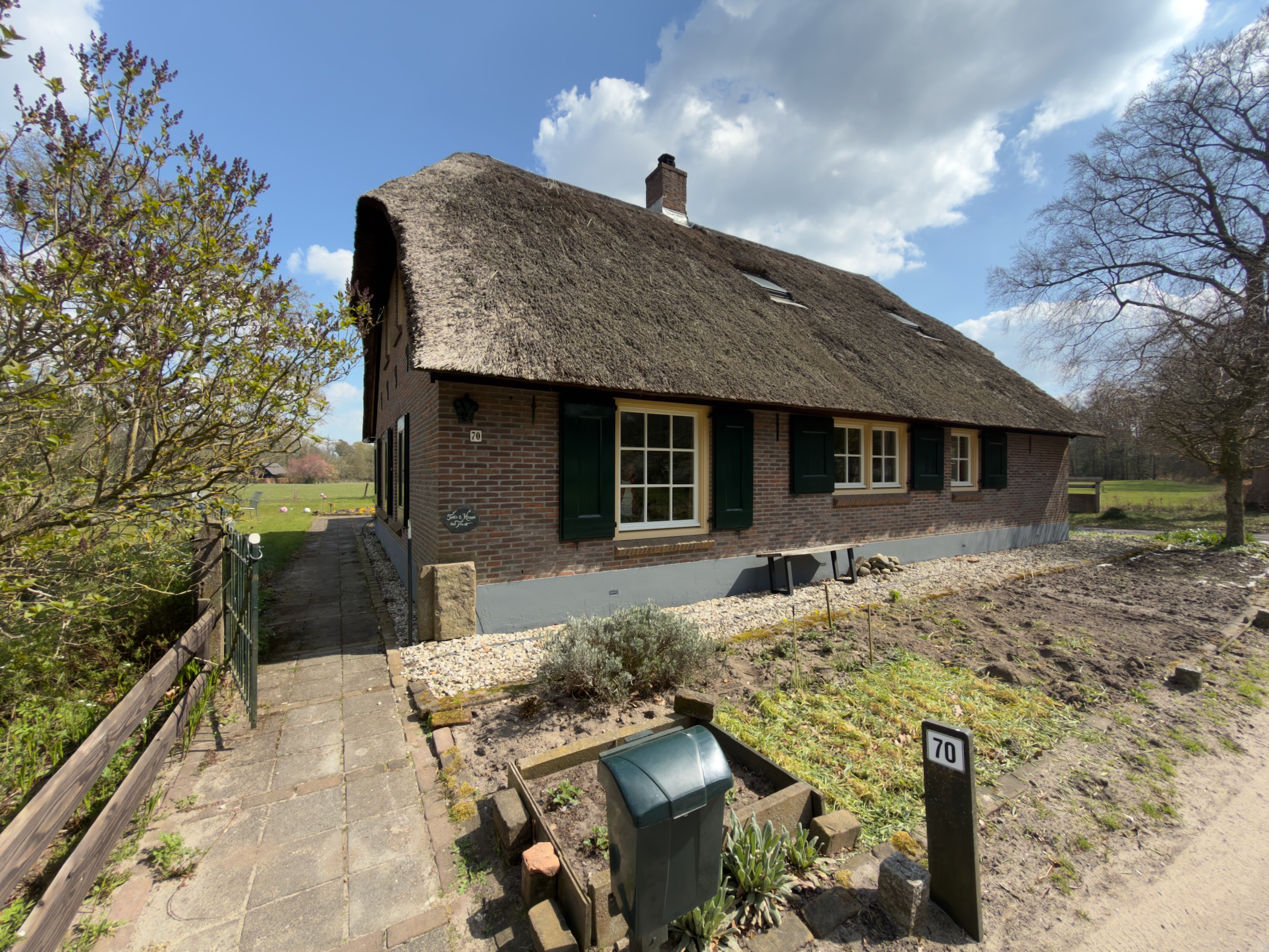 Traditional thatched-roof farmhouse with green shutters and a brick facade