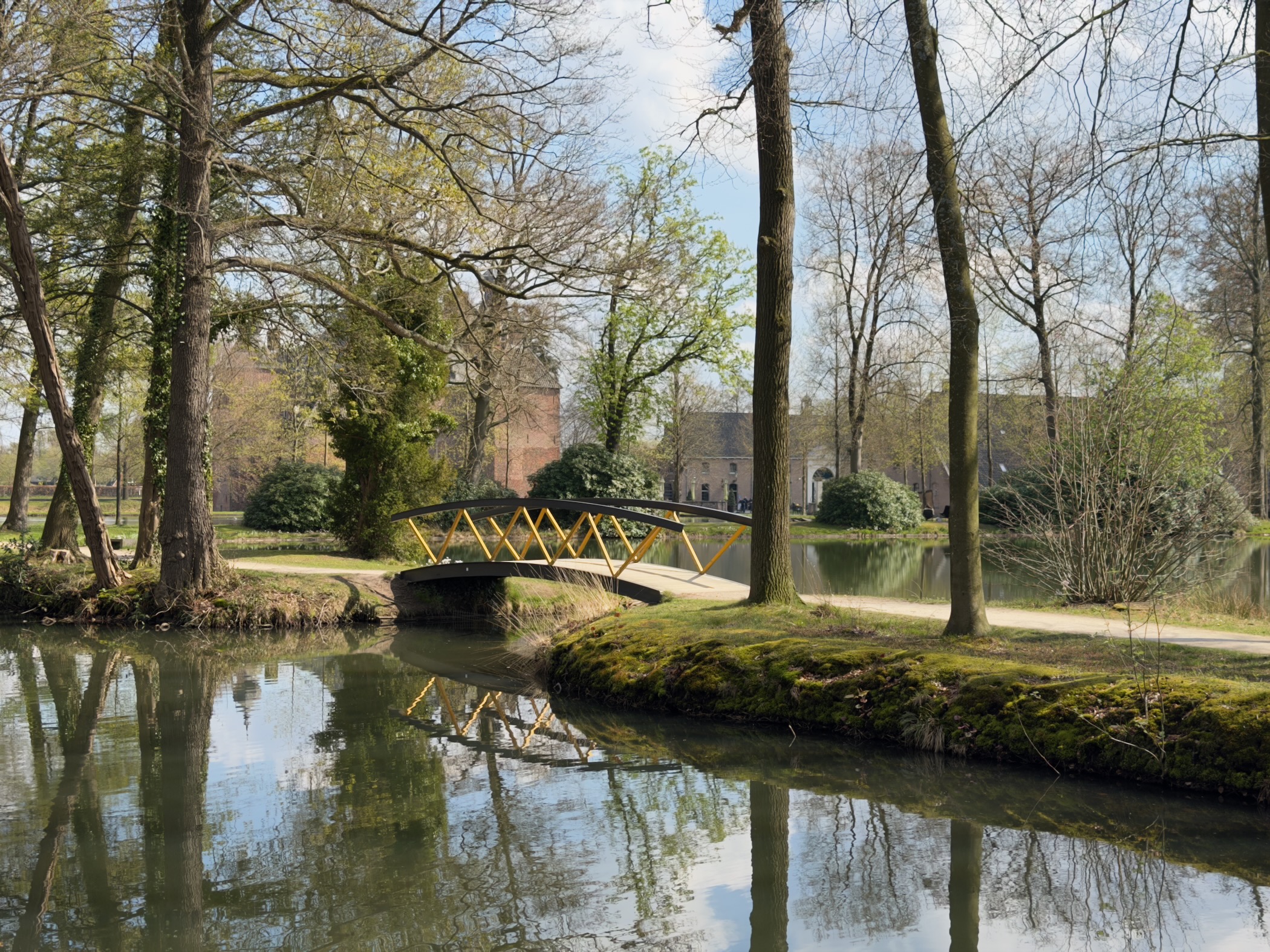 Yellow ornamental bridge over a moat with a castle visible through the trees