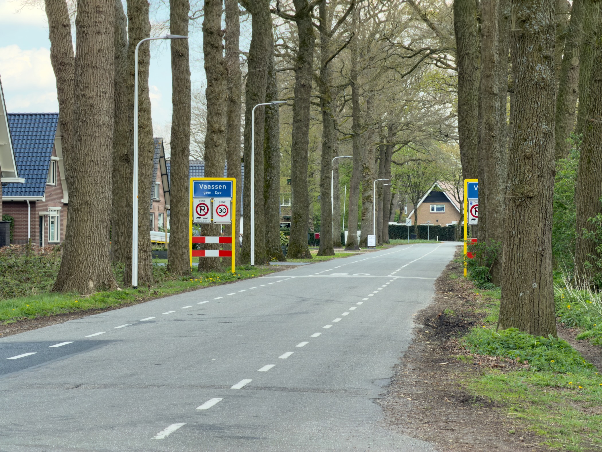 Tree-lined road entering Vaassen with blue and yellow place-name signs