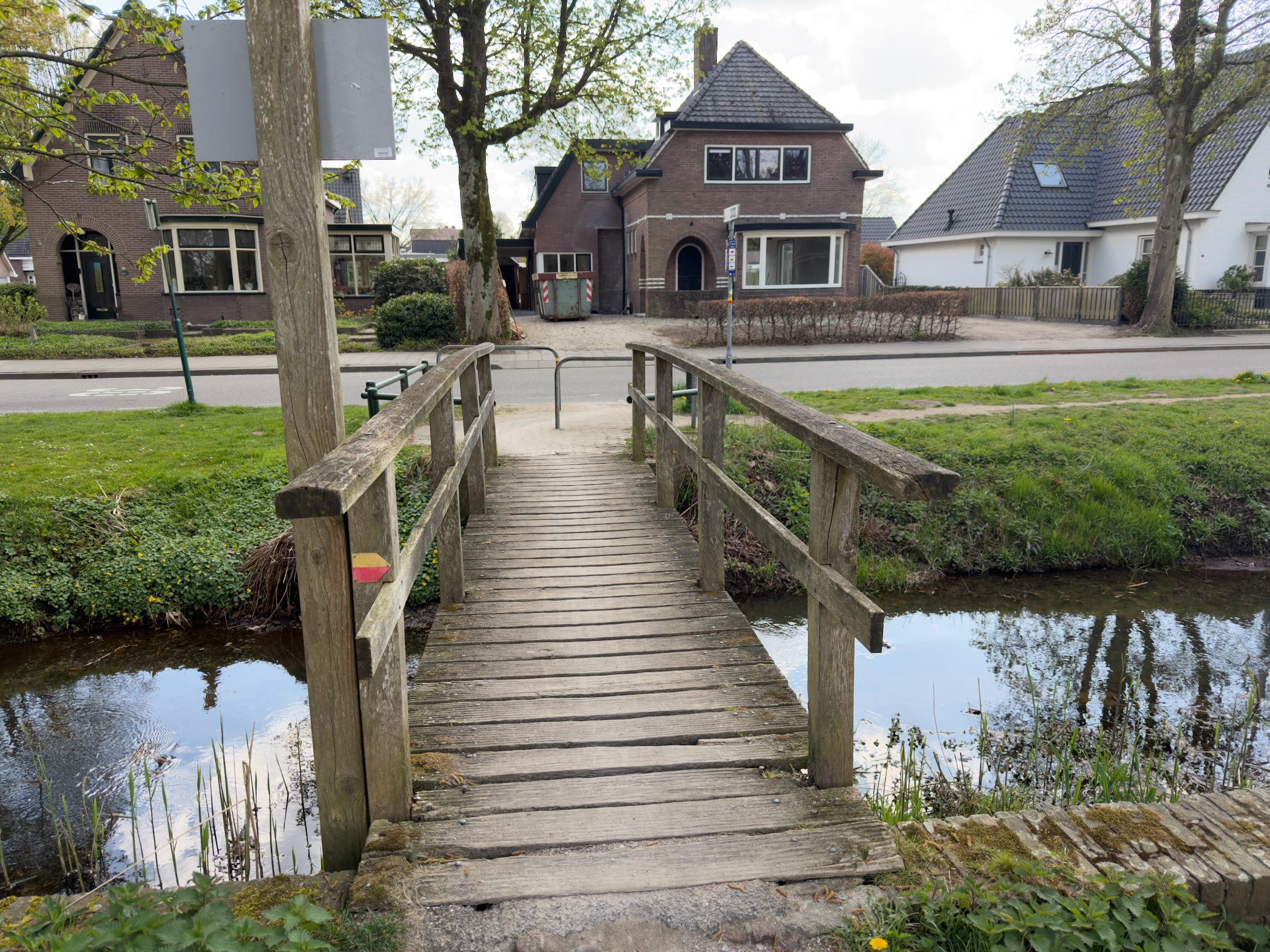 Small wooden footbridge with handrails crossing a canal towards village houses