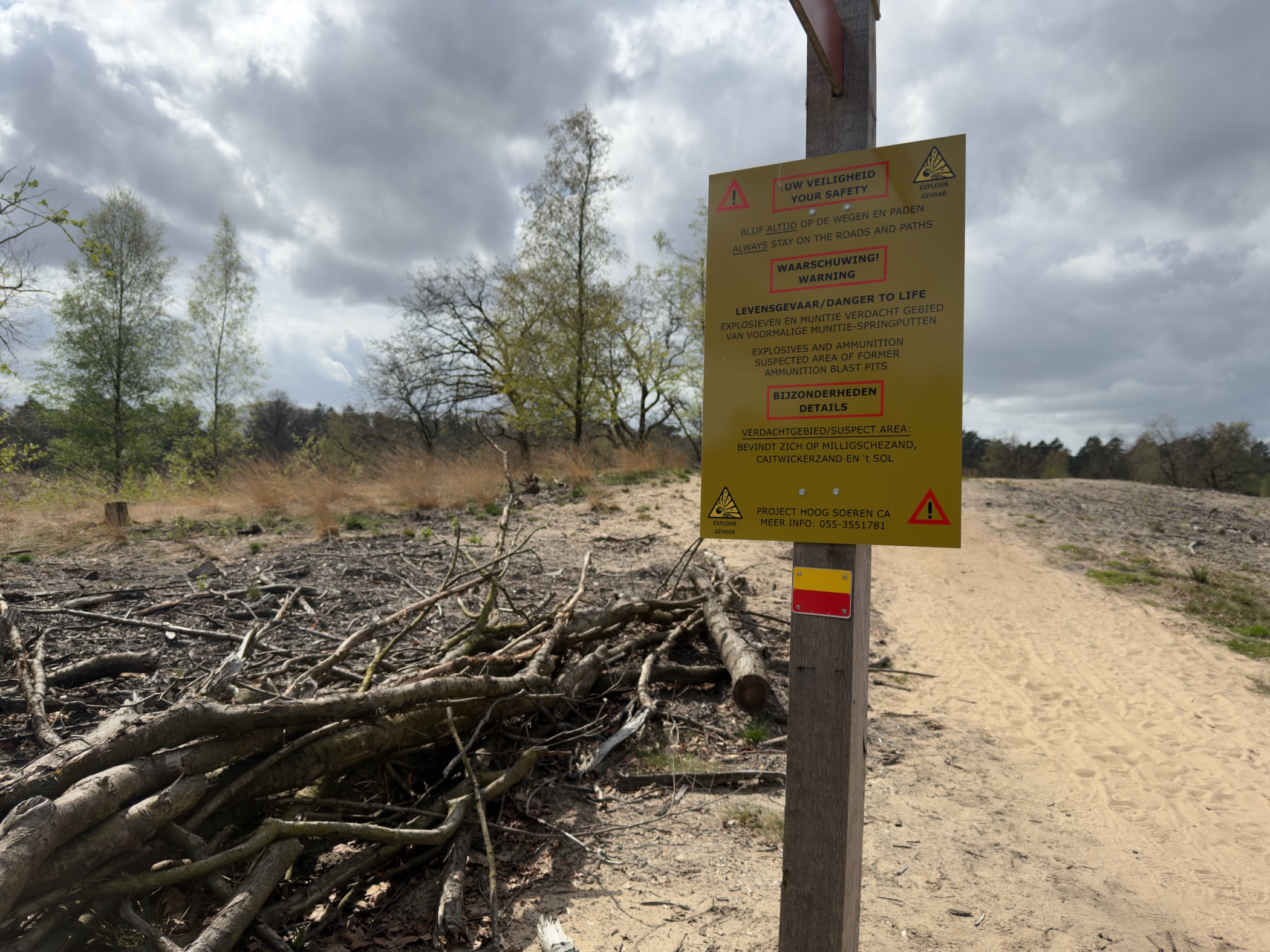 Yellow Dutch warning sign marking a former military shooting area, beside scattered felled branches