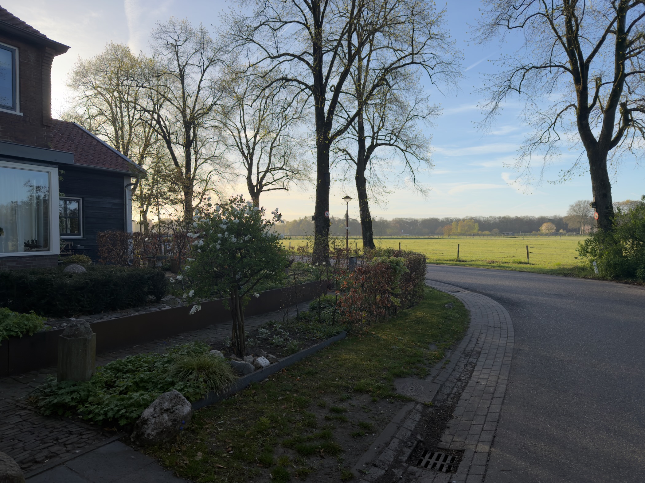 Curved village road with a house and garden overlooking green fields in the morning light