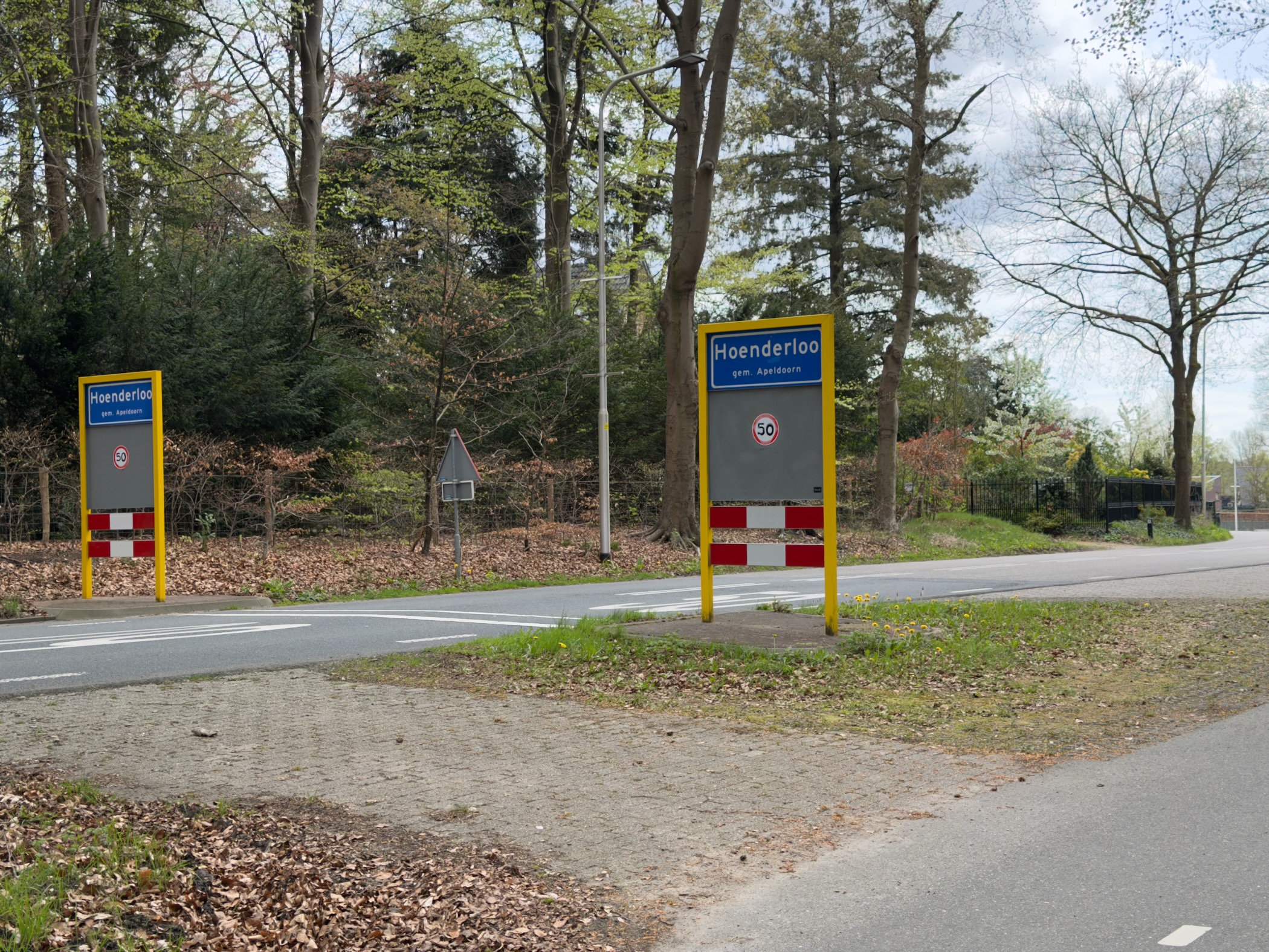 Village signs marking the entrance to Hoenderloo at a road intersection