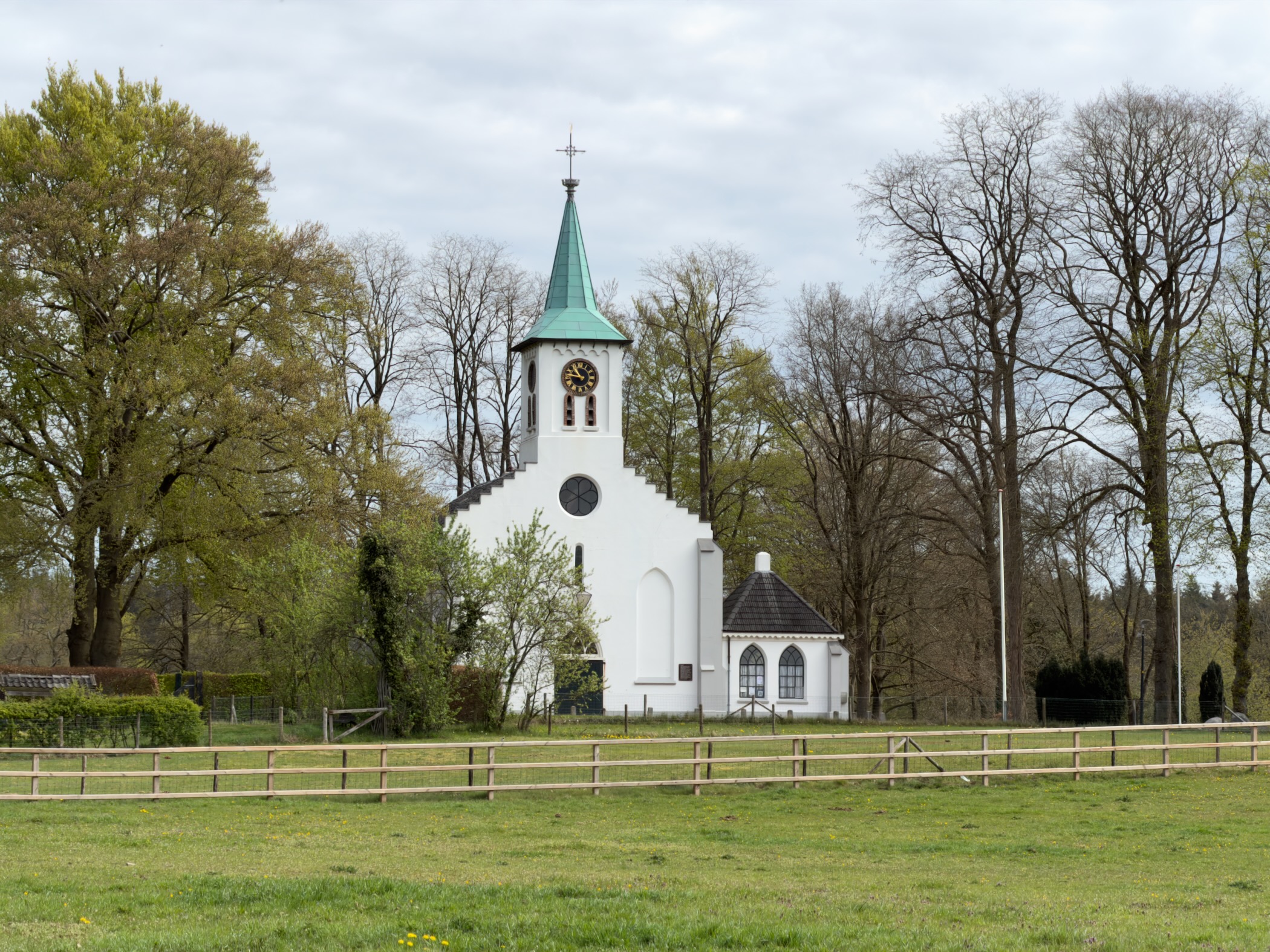 White village church with green steeple and clock behind wooden paddock fencing