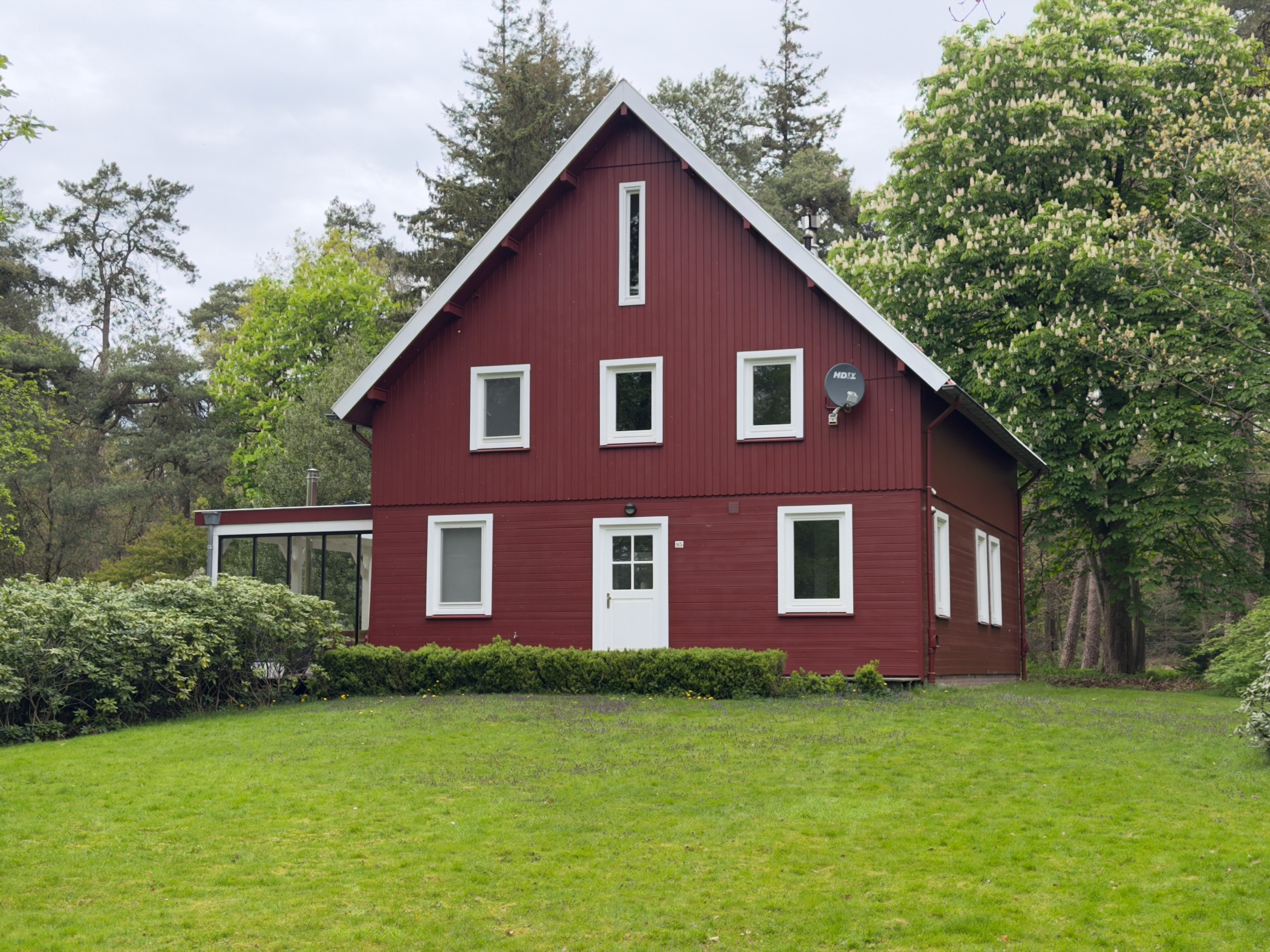 Dark-red wooden house with white trim standing on a grassy clearing in the forest