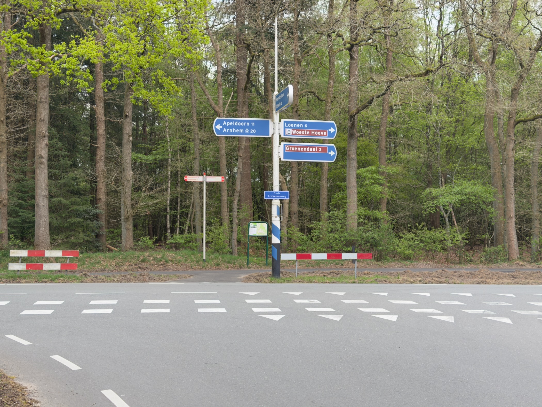 Road crossing with blue directional signs pointing to Apeldoorn, Arnhem and Loenen