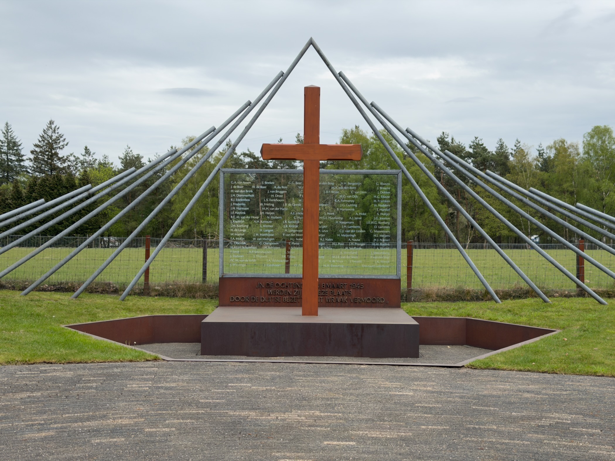 Woeste Hoeve memorial with a wooden cross and radiating steel beams listing victims' names
