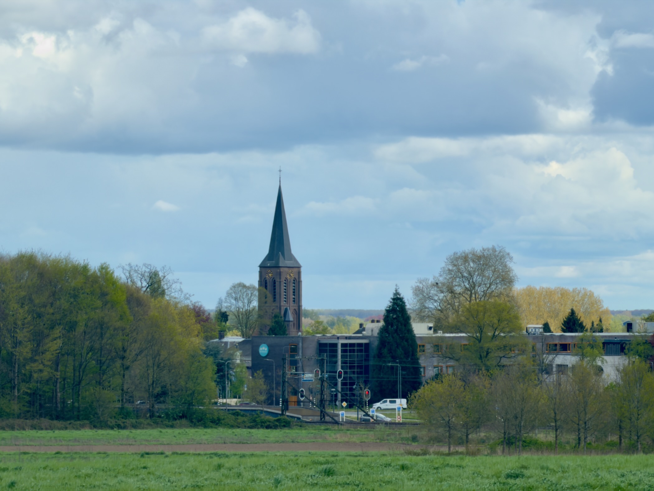 View across fields to the brick church tower of Spankeren under a cloudy sky