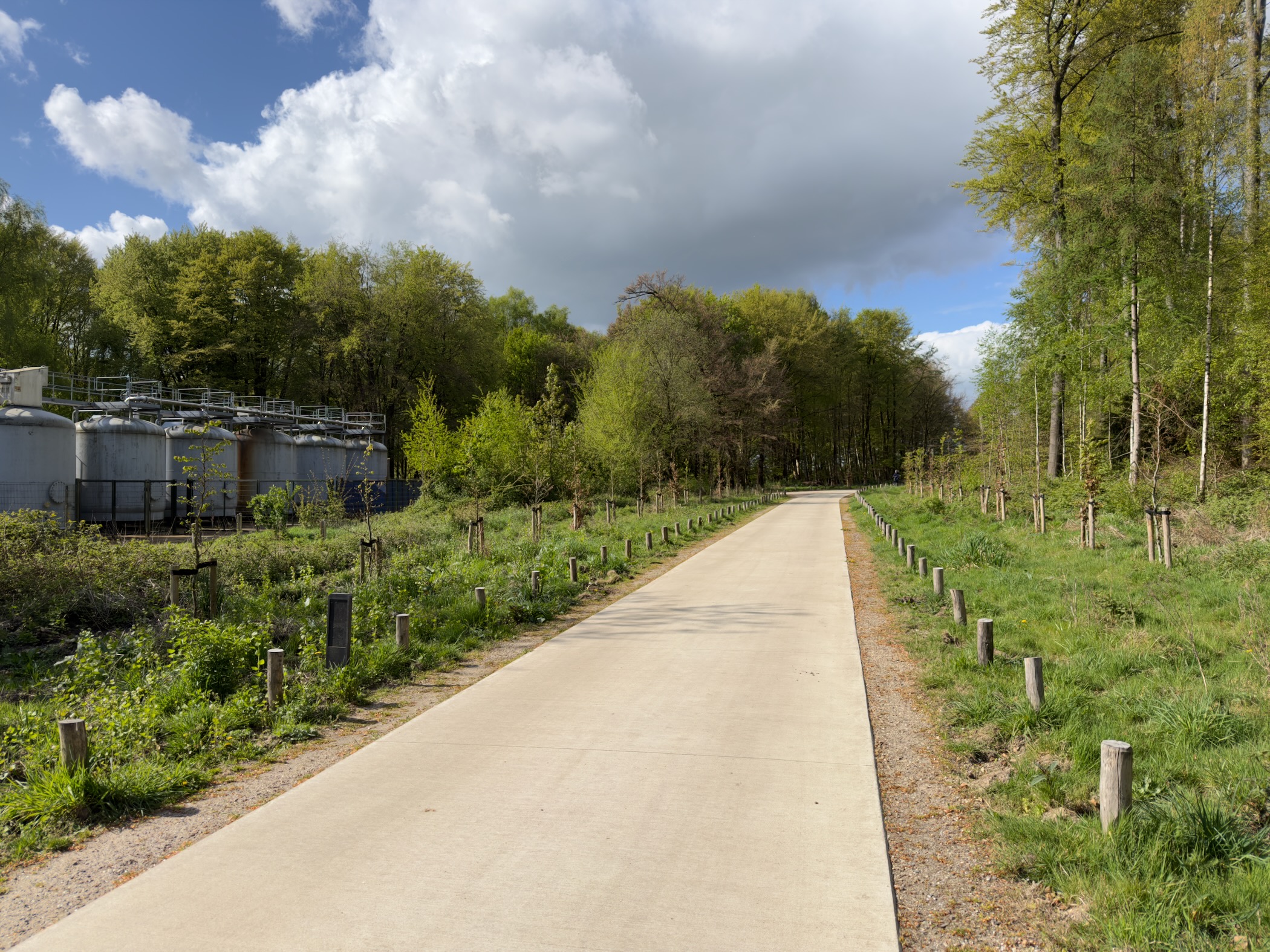 Paved bike path past industrial silos and freshly planted saplings