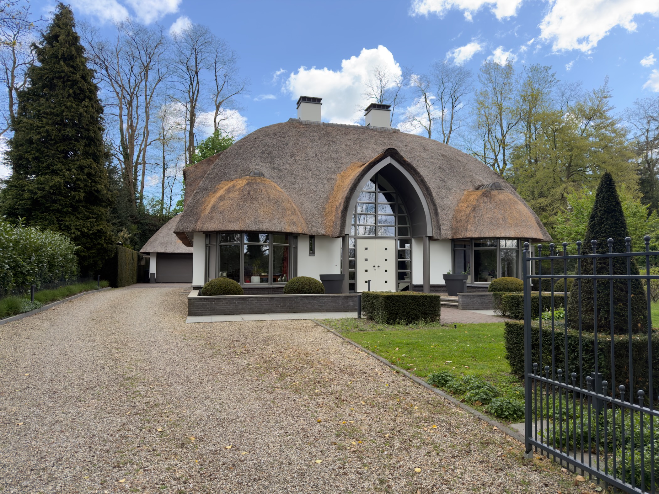 Thatched arched-gabled villa behind a gravel drive and wrought-iron gate in Rheden