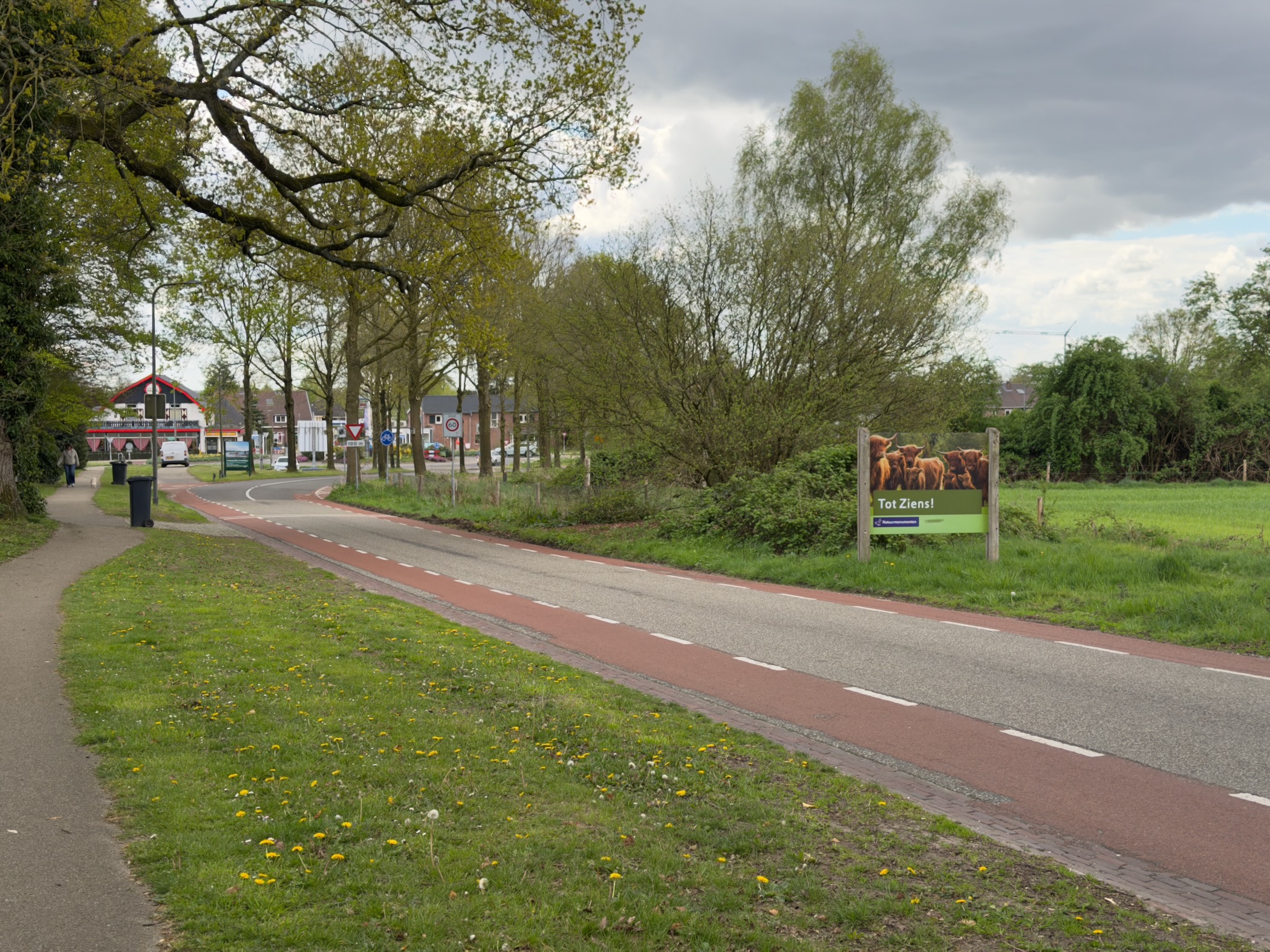 Edge of Rheden village with a red cycling path and a green 'Tot Ziens' sign