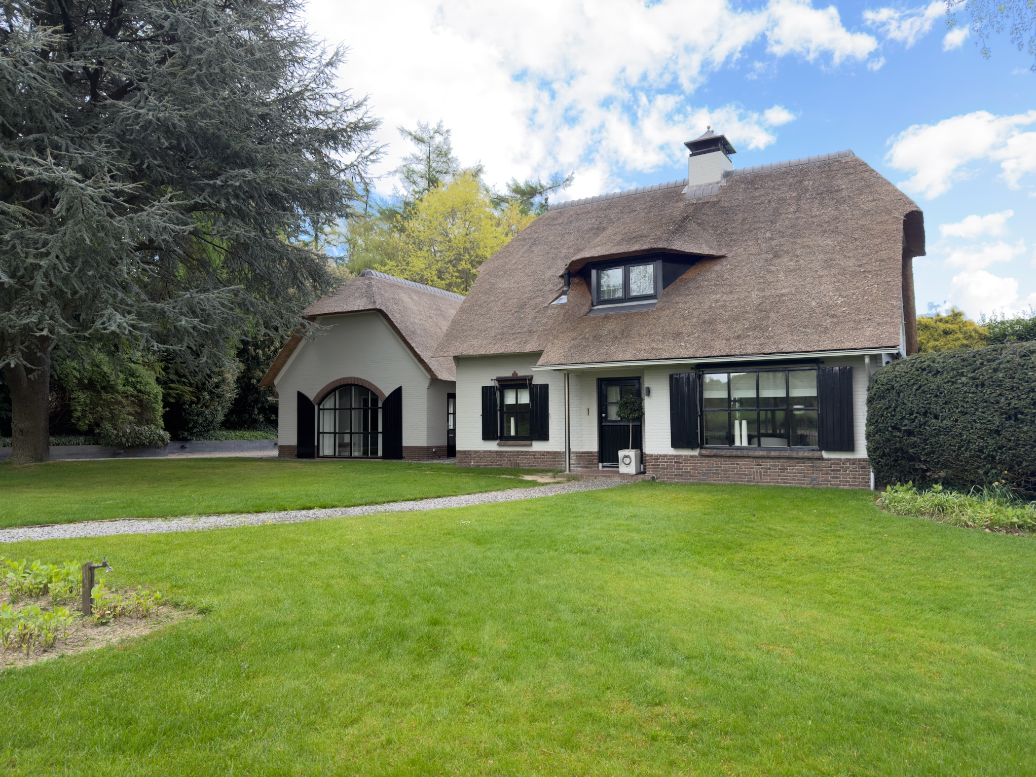 Thatched white country villa with black shutters and a large green lawn