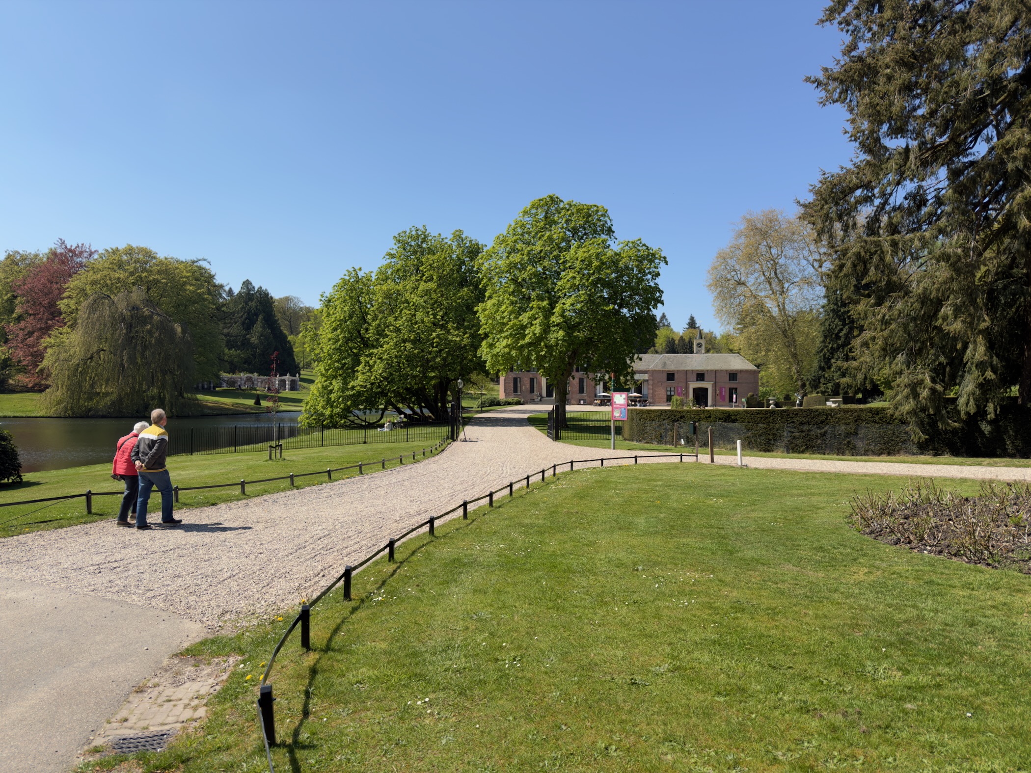 Two visitors on a gravel path by a pond with the outbuildings of Castle Rosendael behind