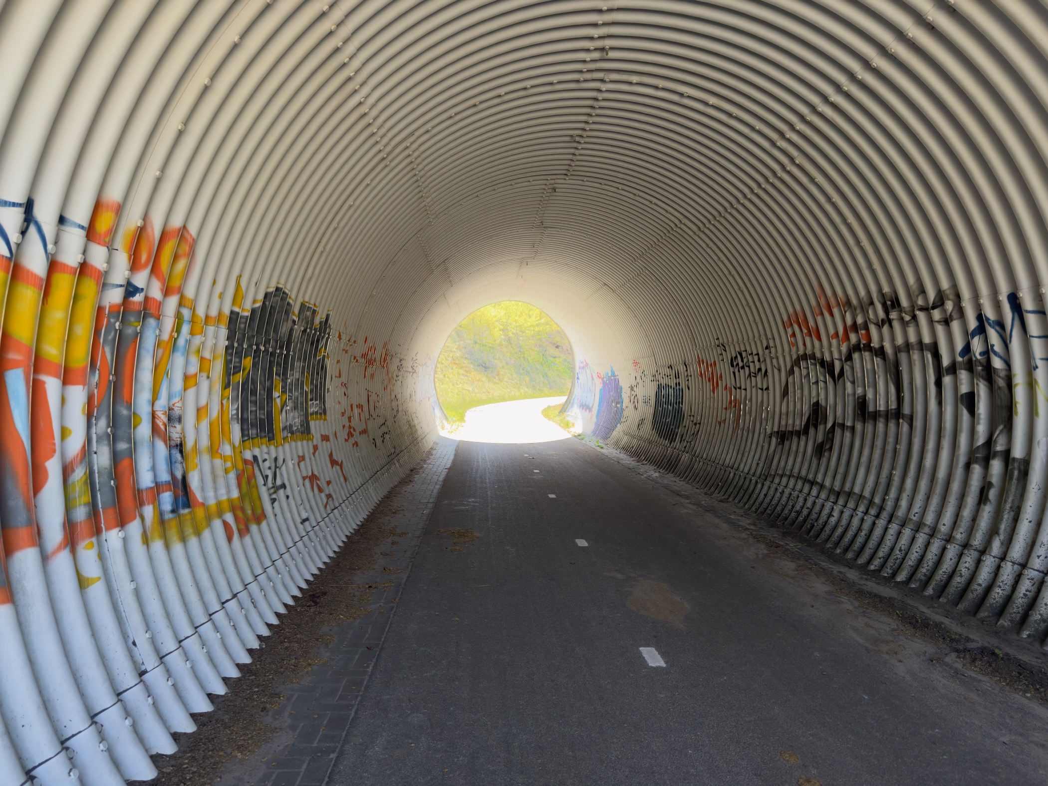 Inside a corrugated tunnel covered in graffiti with daylight at the far end