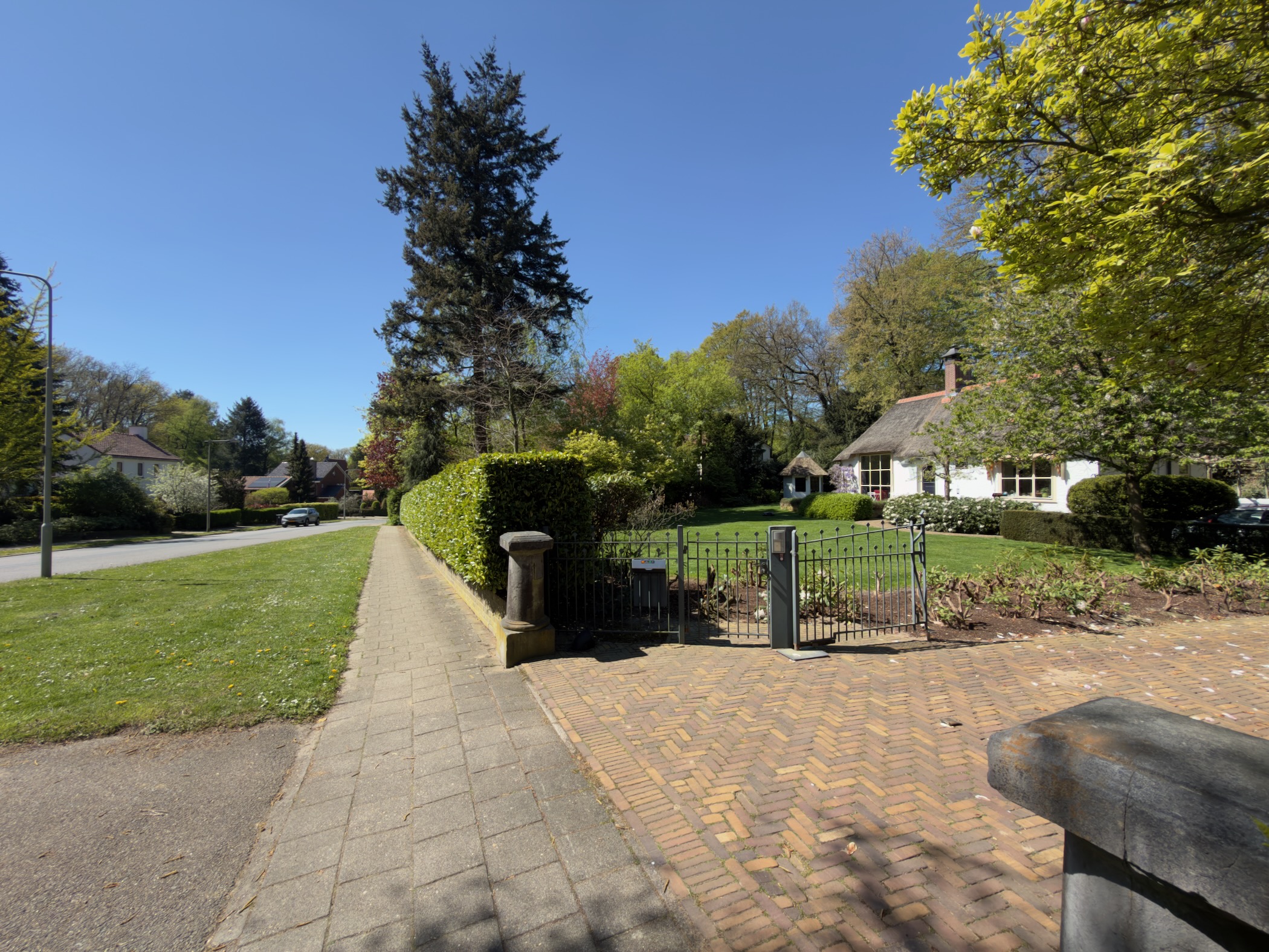 Pavement passing a clipped hedge and gate in front of a thatched white cottage