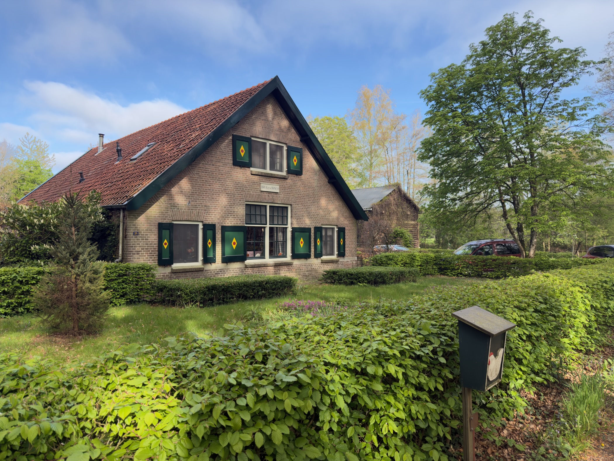 Traditional Veluwe farmhouse with green-shuttered windows behind a clipped hedge