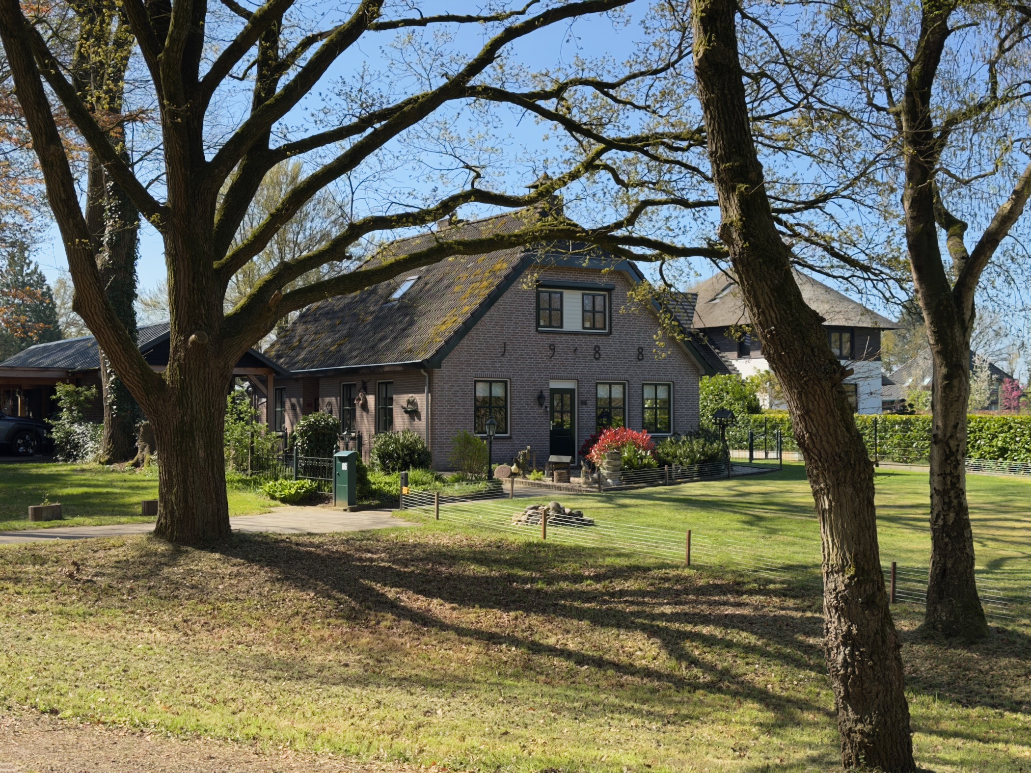 Brick farmhouse dated 1788 seen between the trunks of old oaks on a lawn