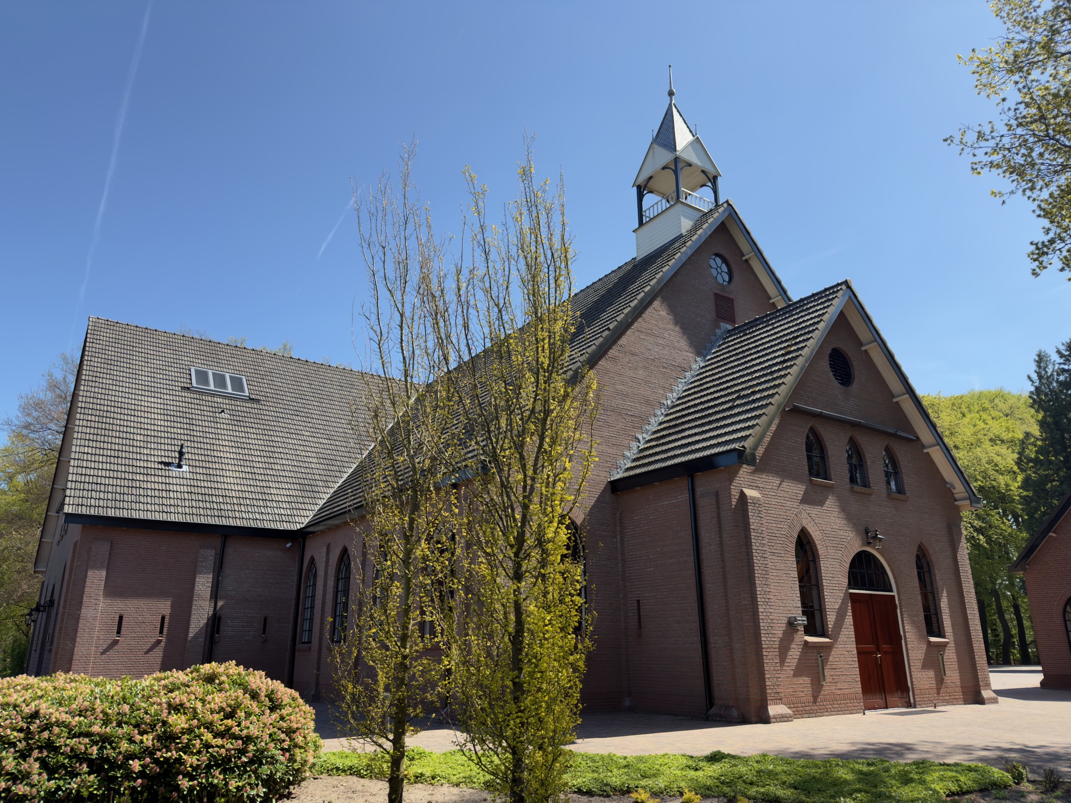 Red brick chapel with a slate roof and bell tower beside a lawn