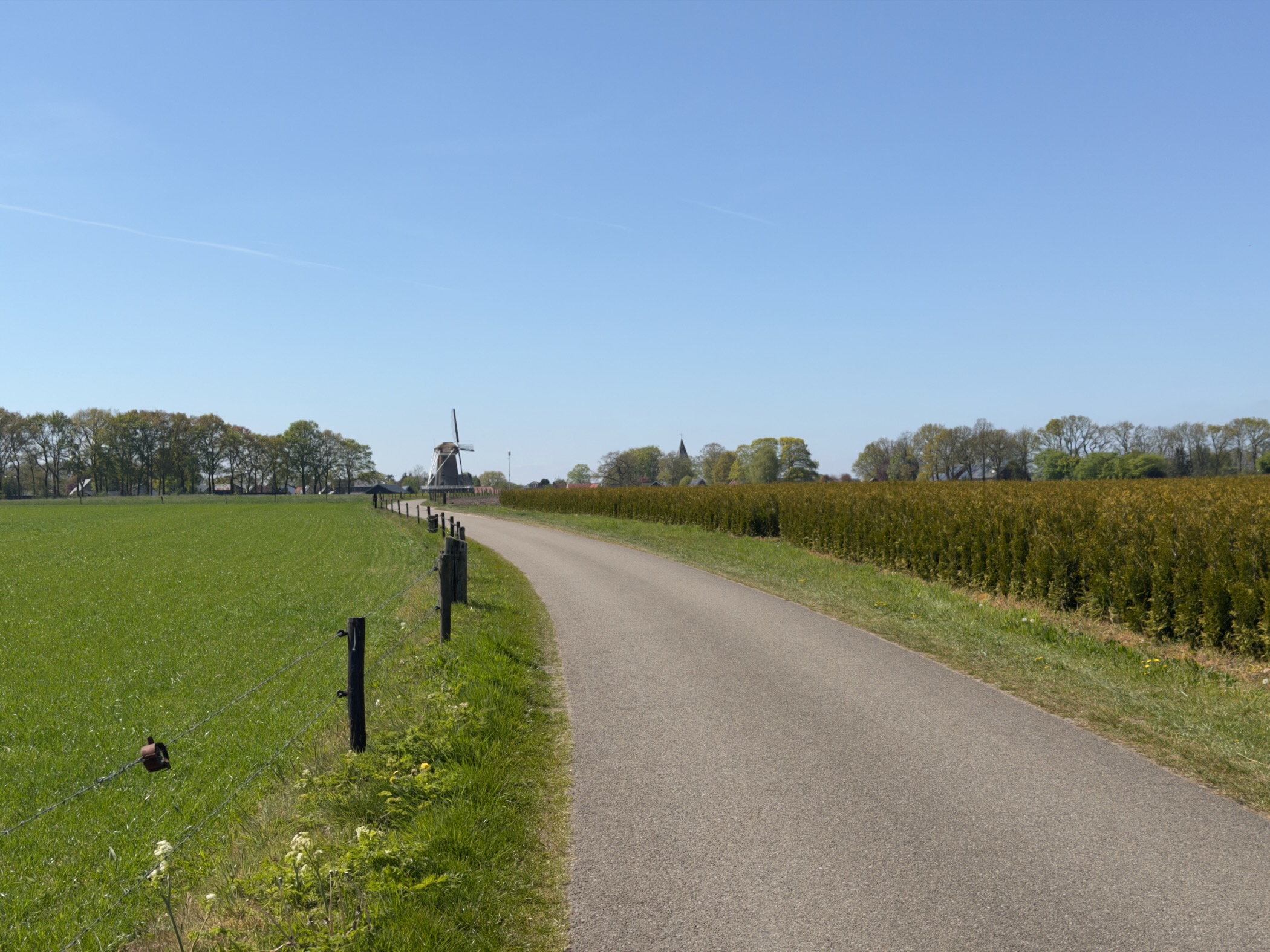 Country lane with a windmill and church tower ahead across a green field