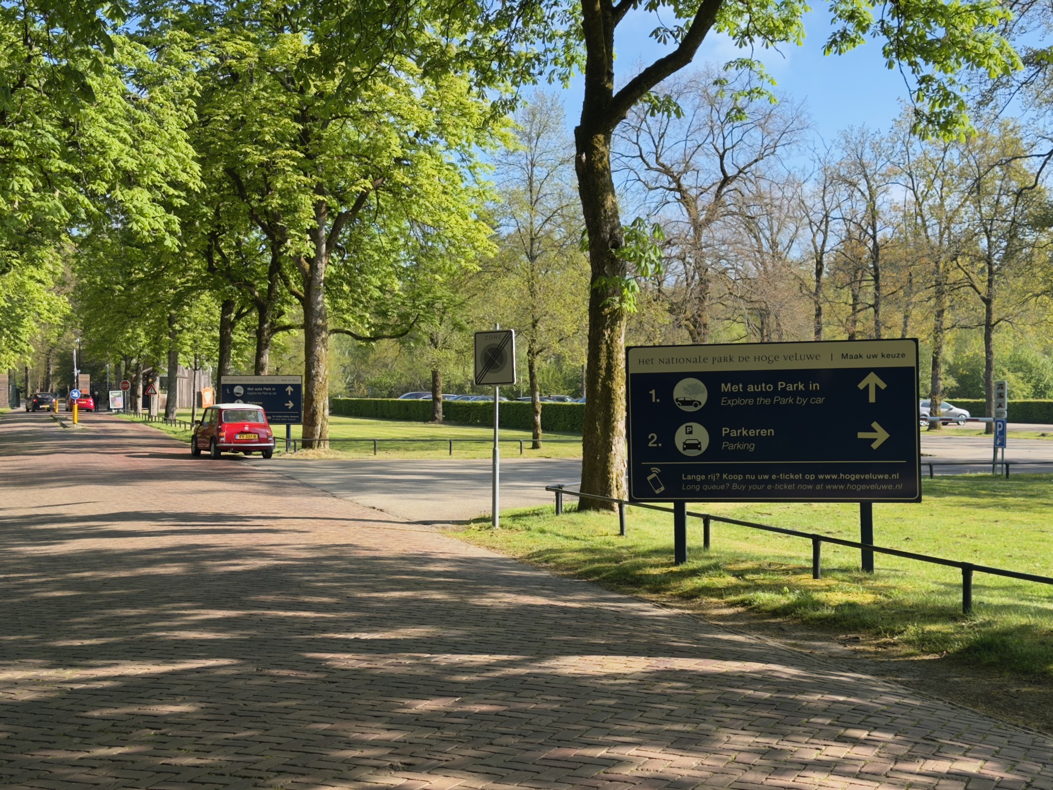 A park entrance with a parking sign and a red car