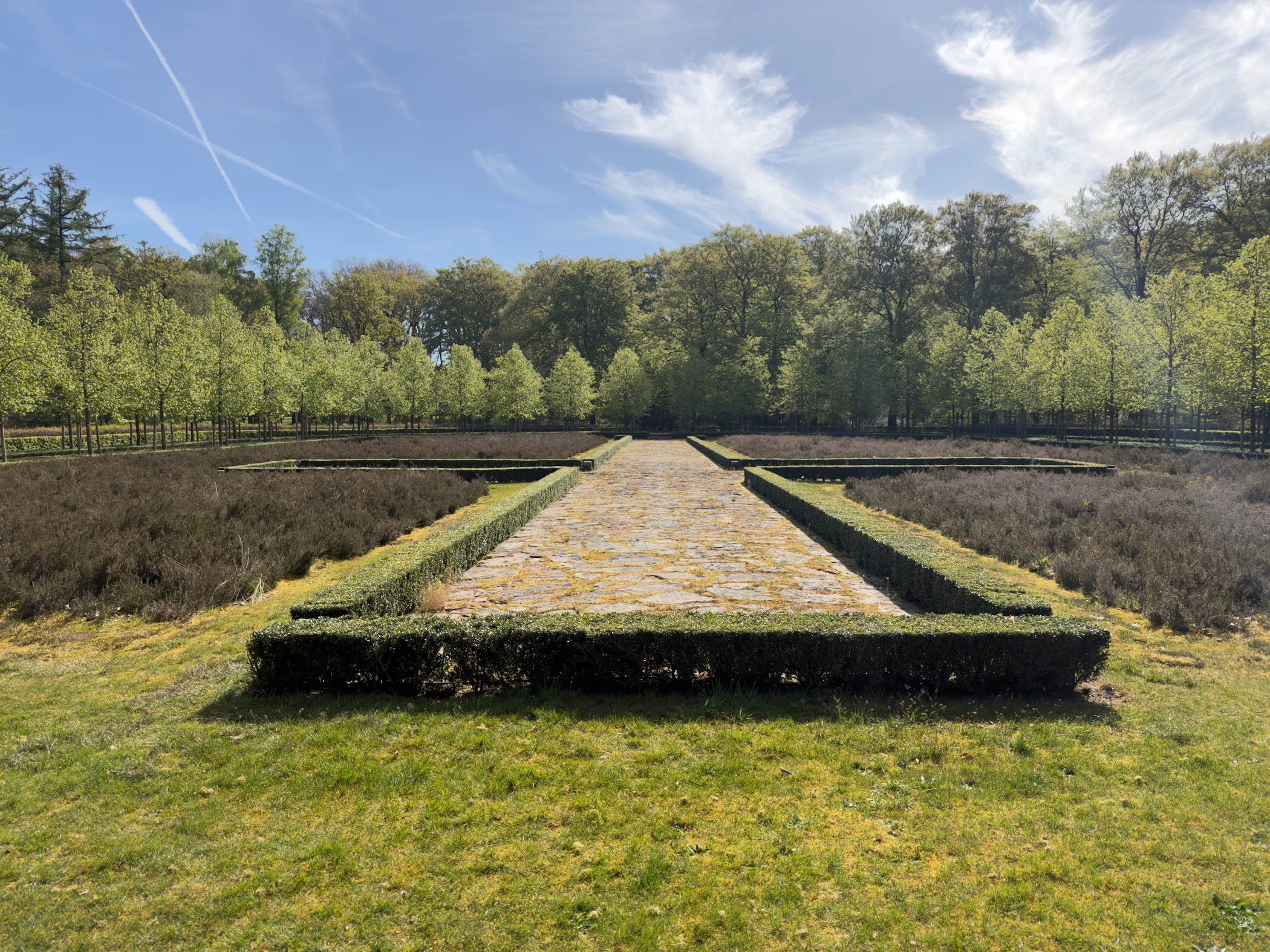 Stone path between low hedges in a sunken garden ringed by trees