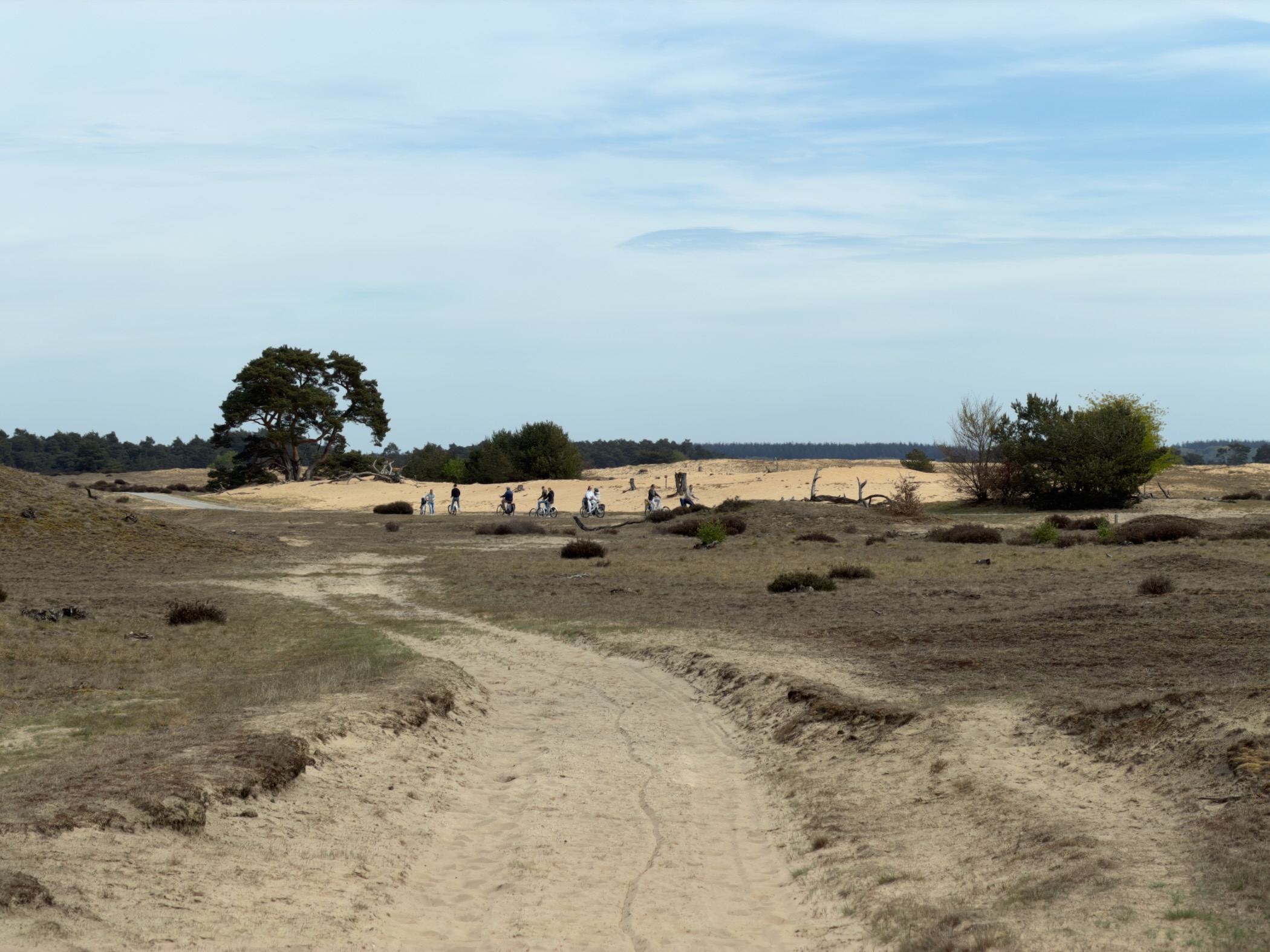 People with bicycles crossing a sandy area near a low ridge